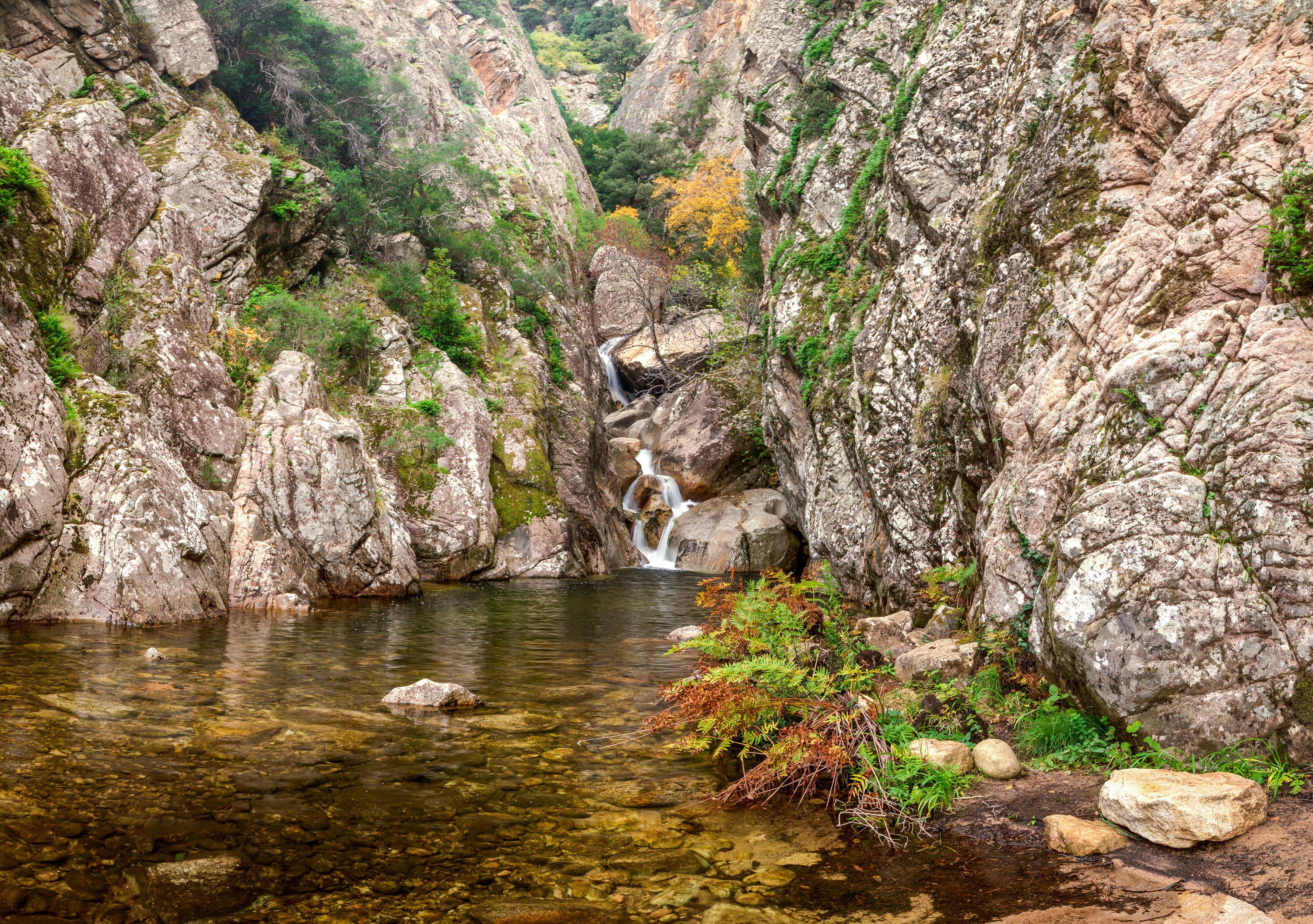 Waterfall cascading into a pool surrounded by rocky cliffs in Corsica, France HD Wallpaper