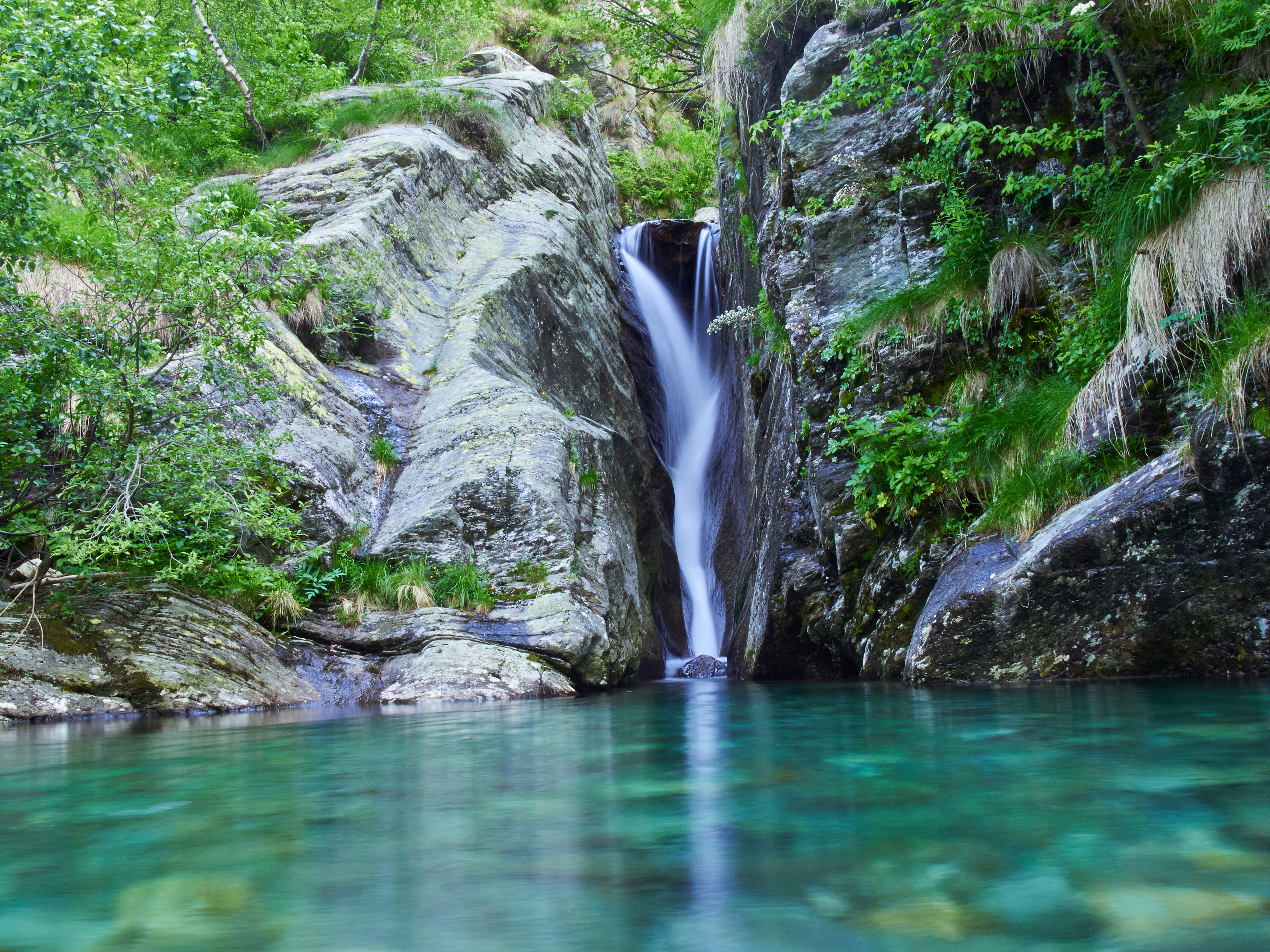 Waterfall cascading into a clear turquoise pool surrounded by rocks and greenery HD Wallpaper