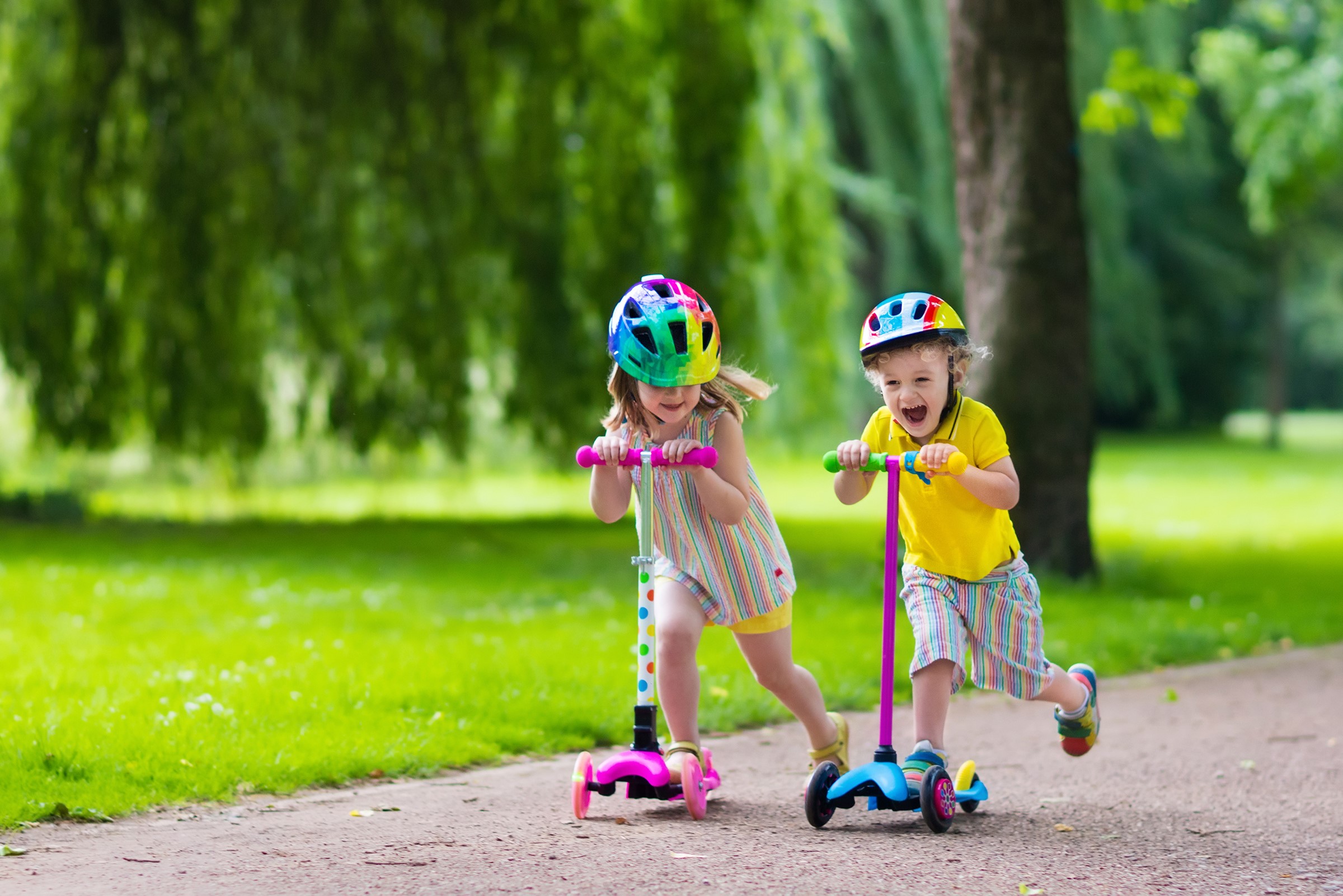 Two children riding scooters in a park HD Wallpaper