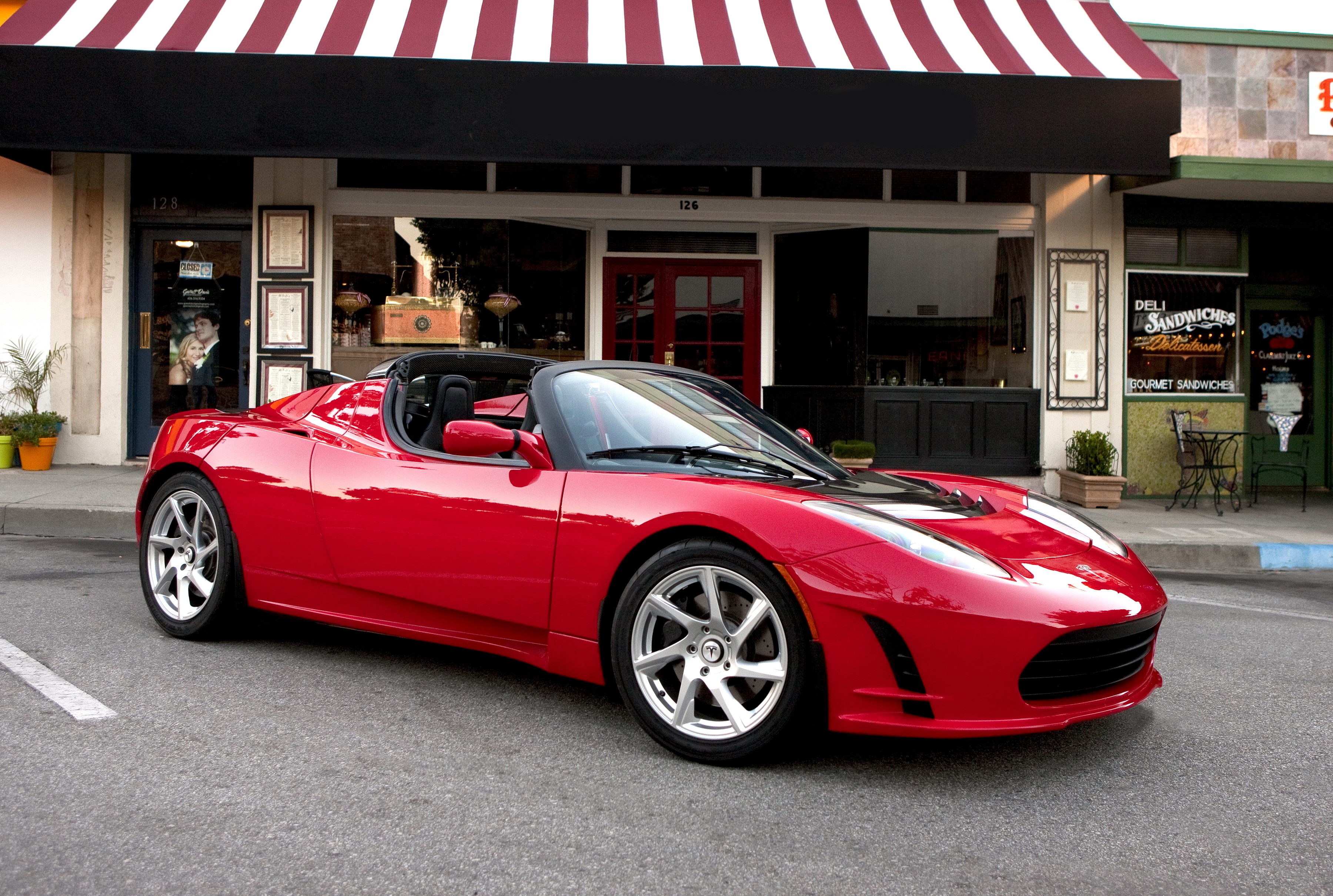 Red Tesla Roadster Sport parked in front of a deli HD Wallpaper