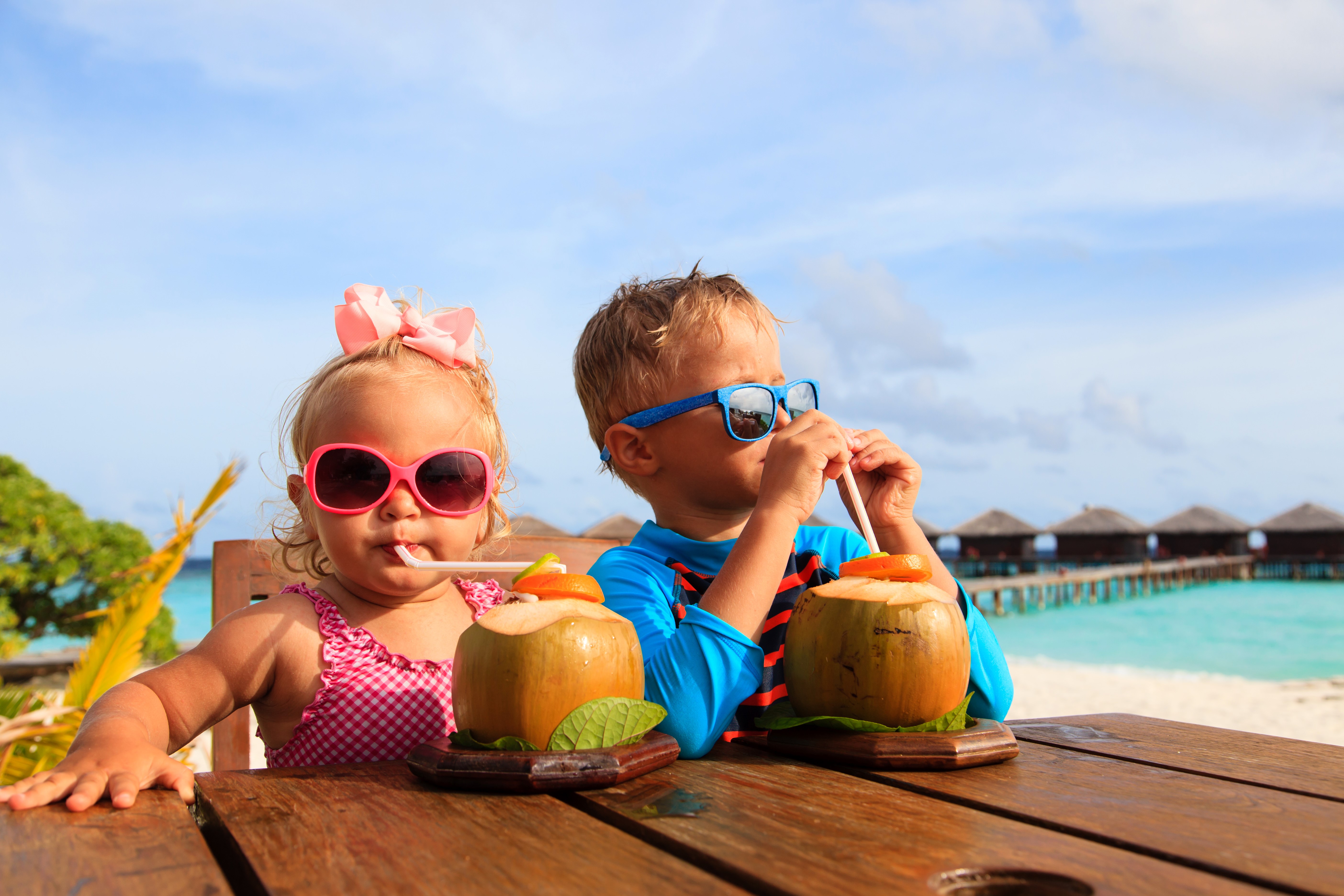 Two children drinking coconut water on a tropical beach HD Wallpaper