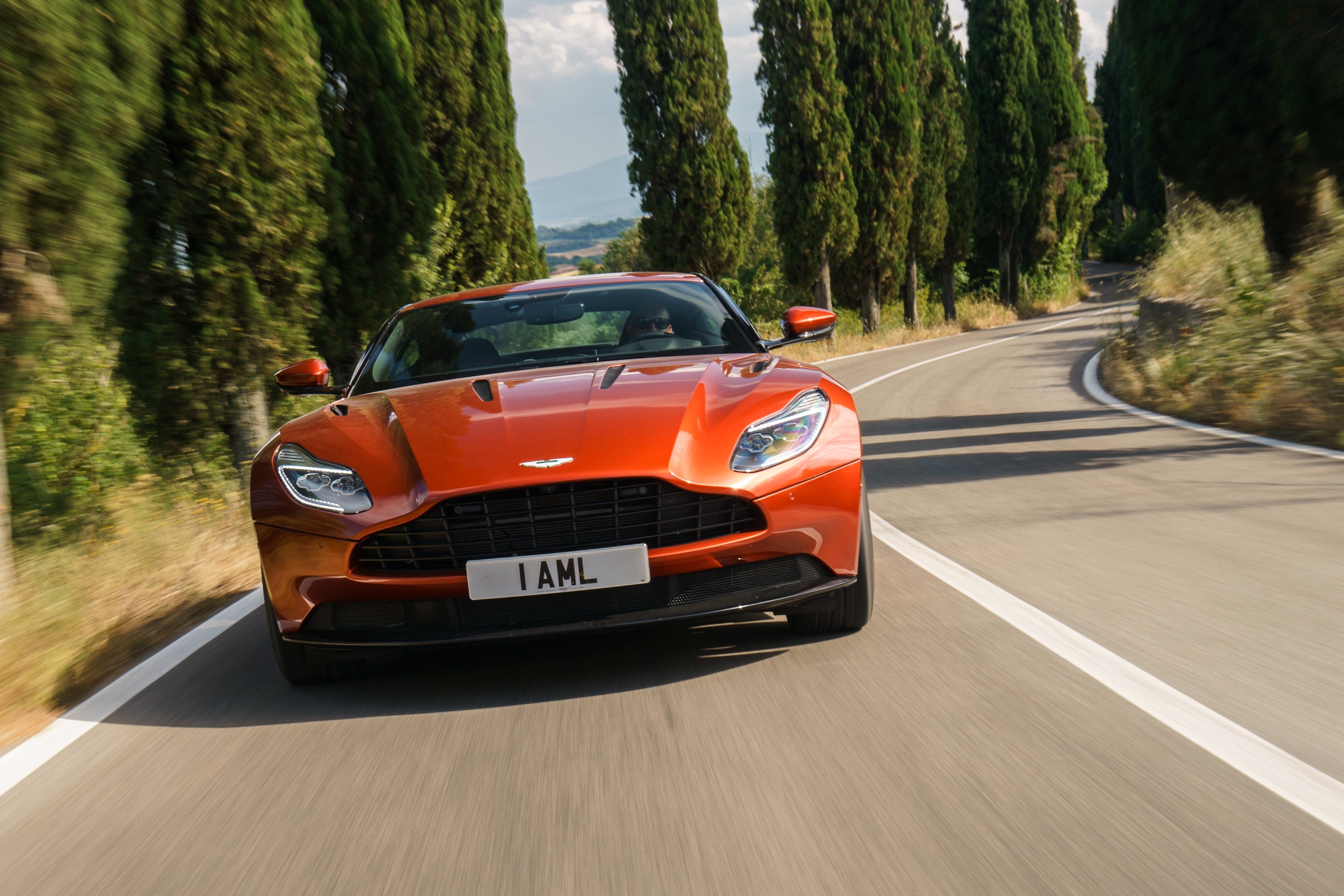Orange Aston Martin DB11 Driving on a Road HD Wallpaper