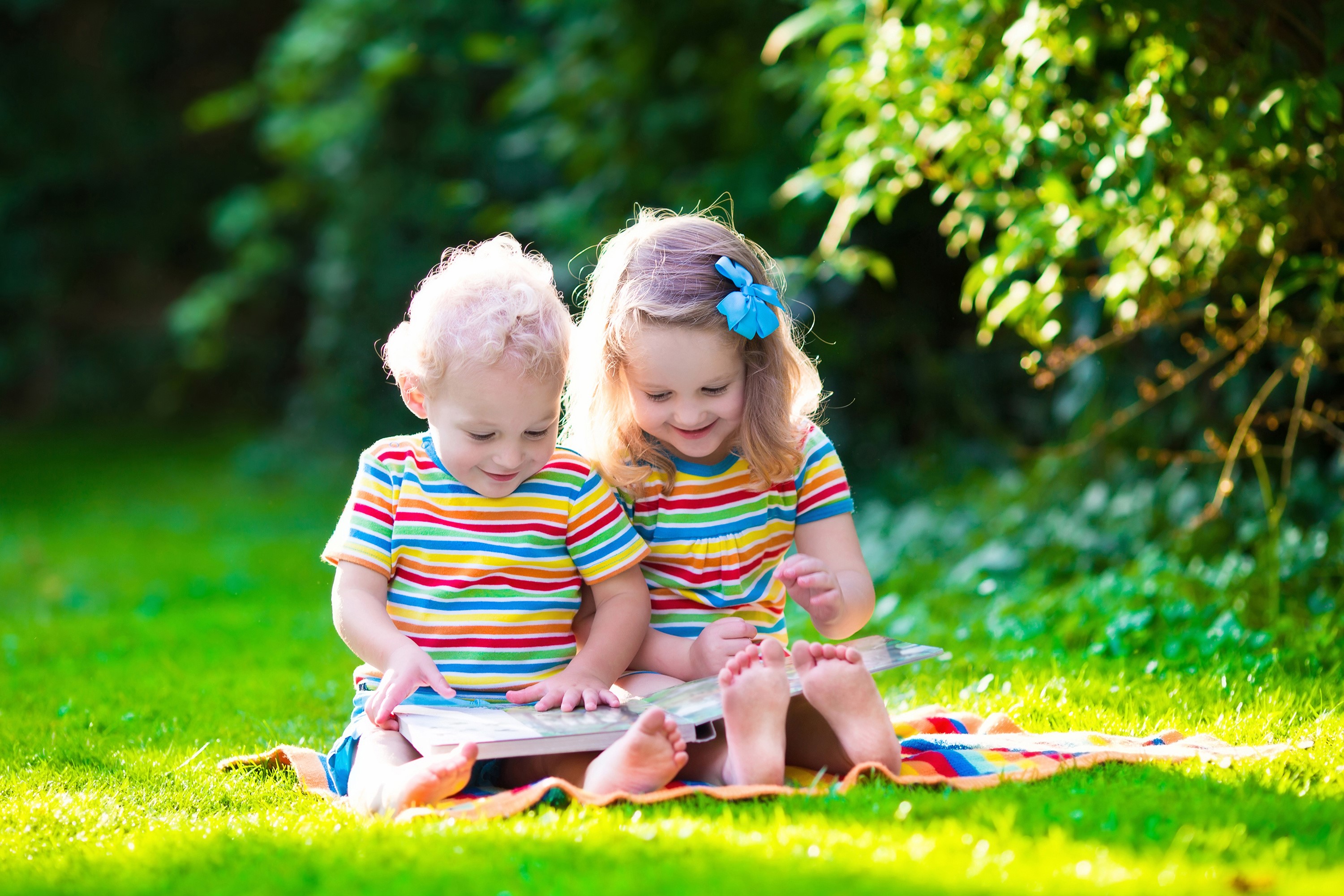 Two children reading a book on a blanket in the grass HD Wallpaper