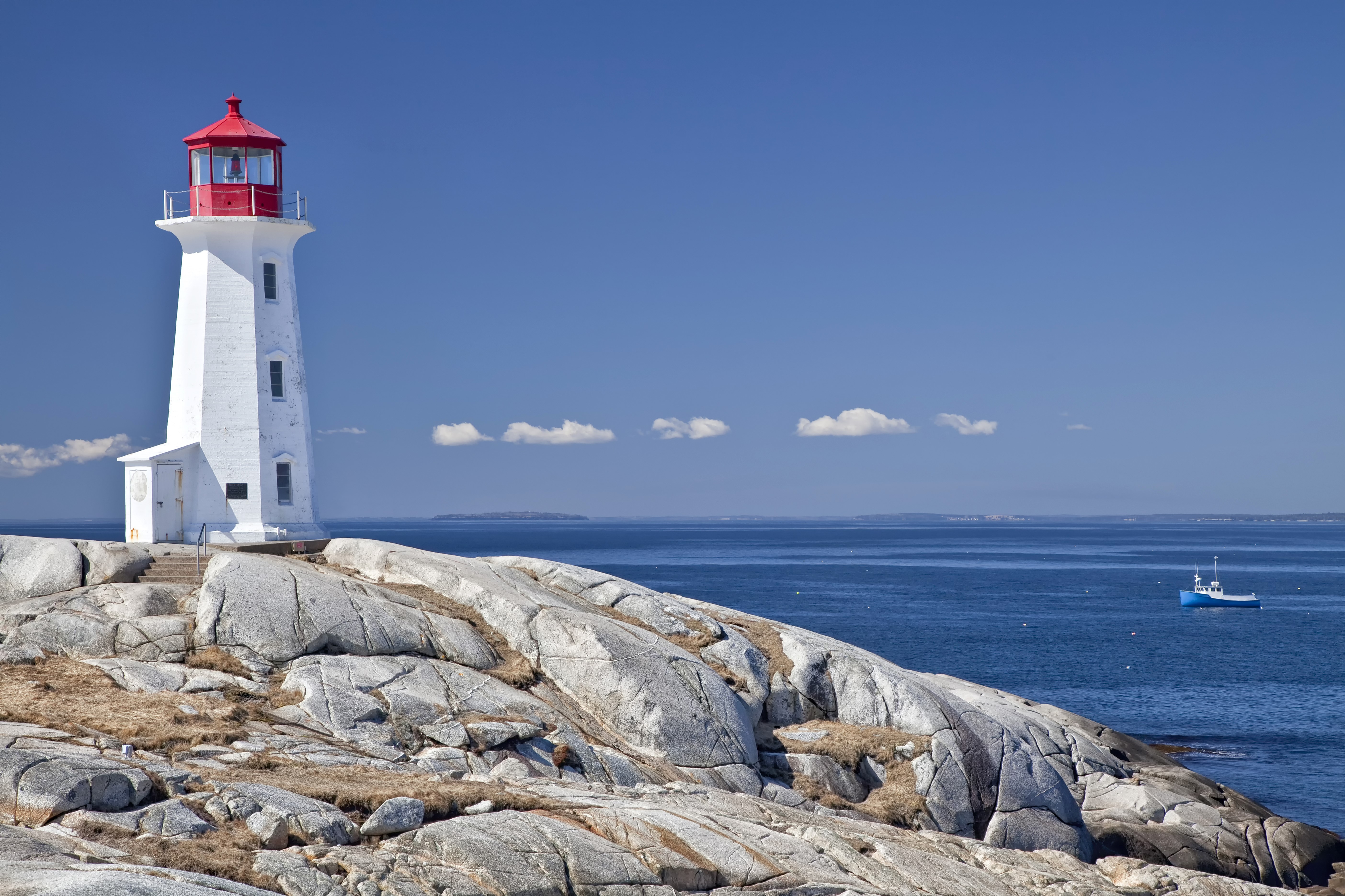White lighthouse on rocky shore with blue ocean HD Wallpaper