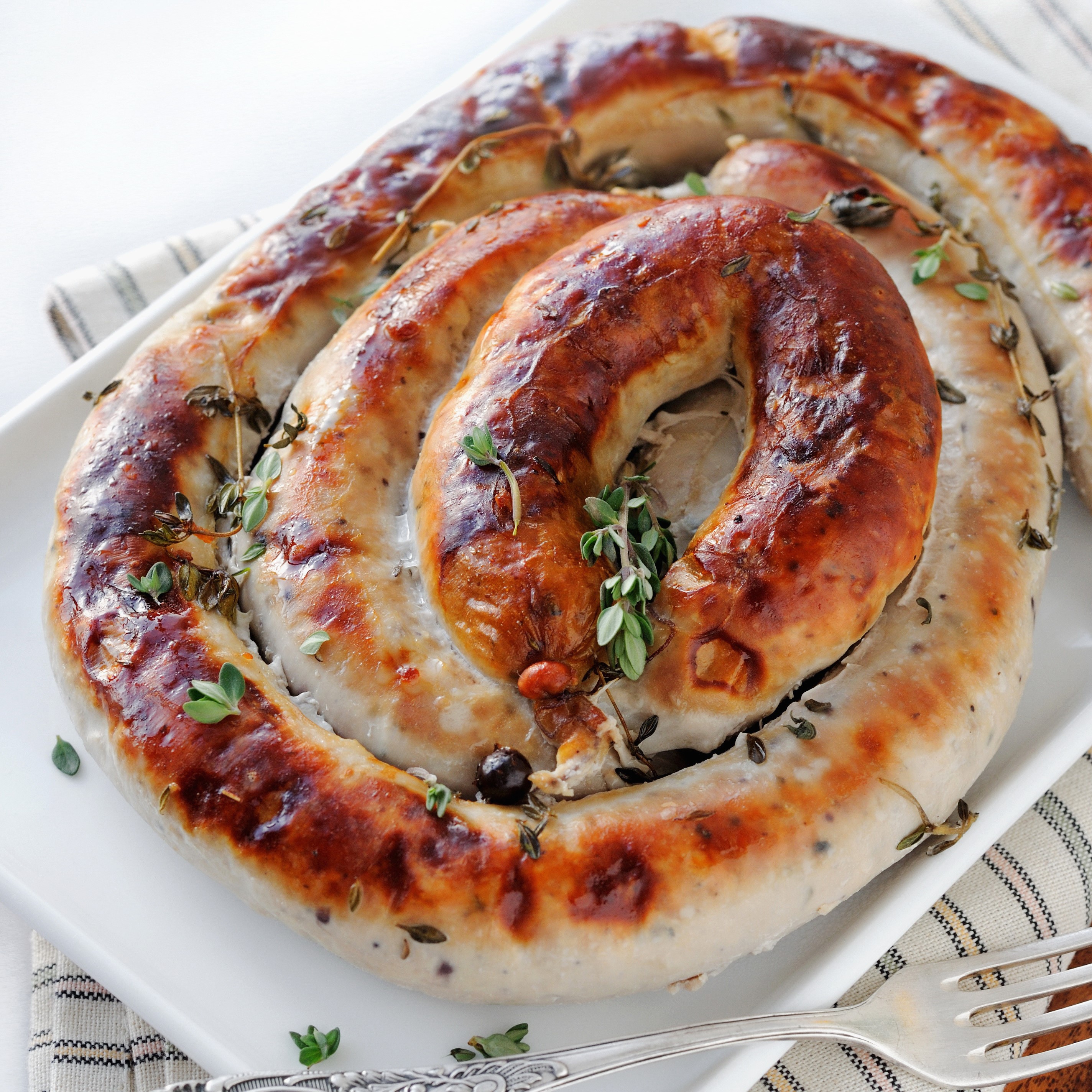 Spiral-cooked sausage with herbs on a white plate HD Wallpaper