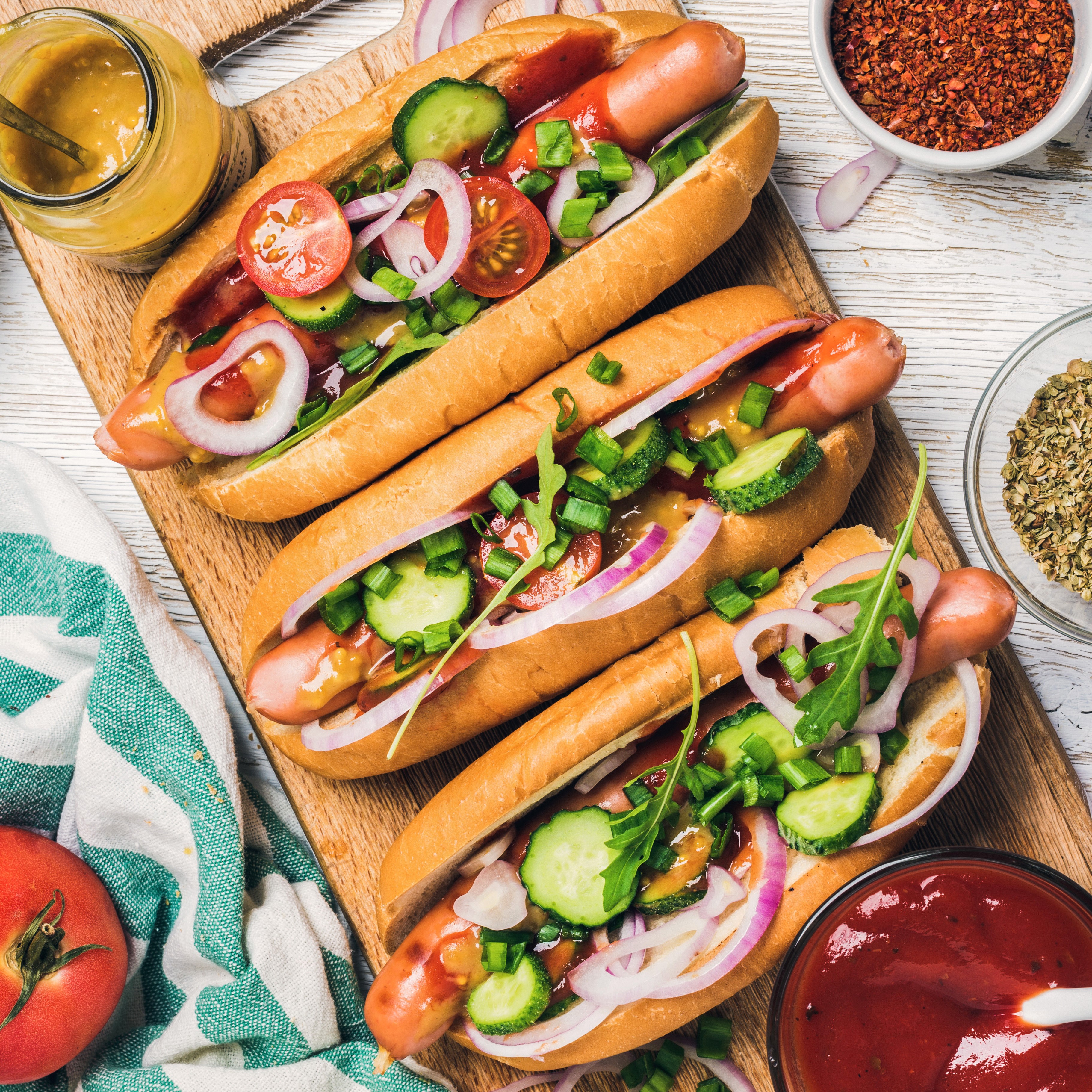 Three hot dogs with toppings on a wooden board HD Wallpaper