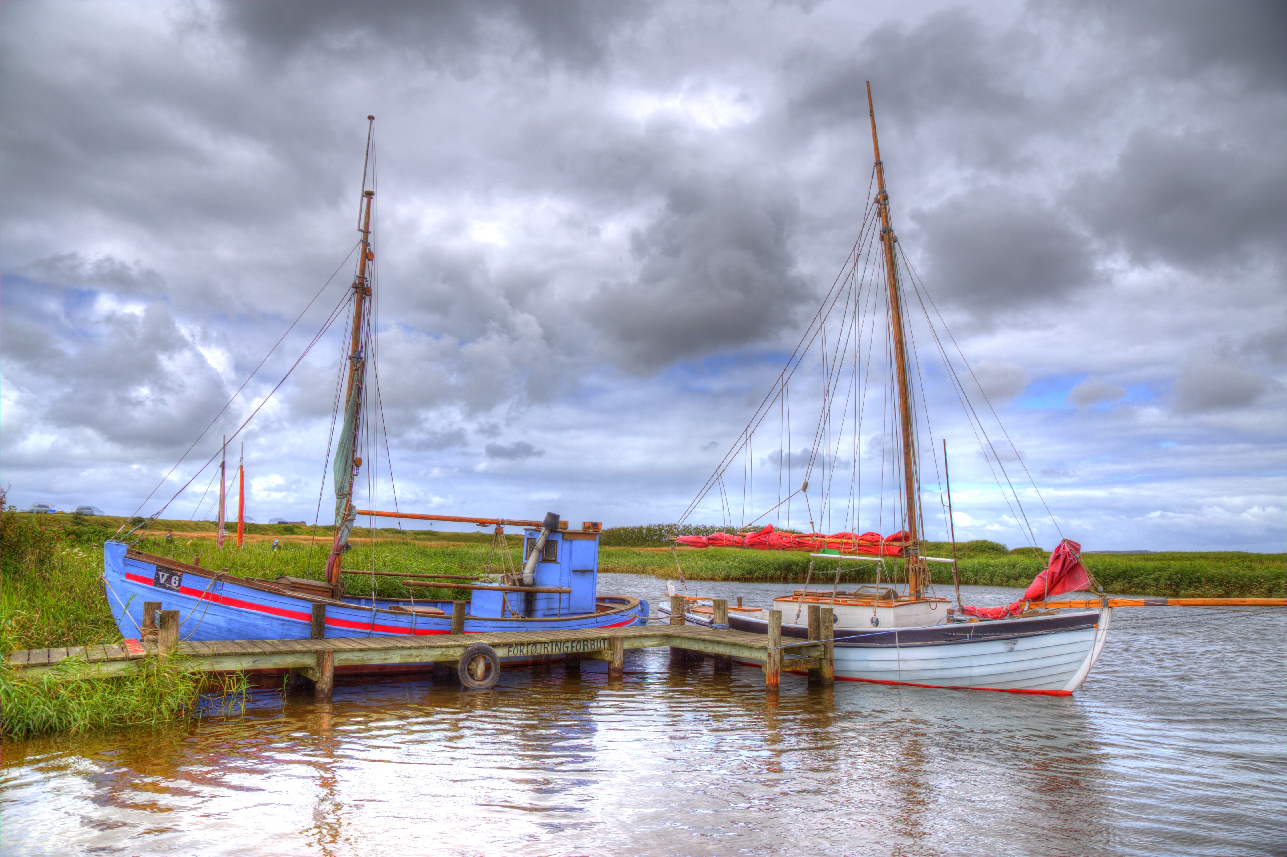 Boats docked on a river under a cloudy sky HD Wallpaper
