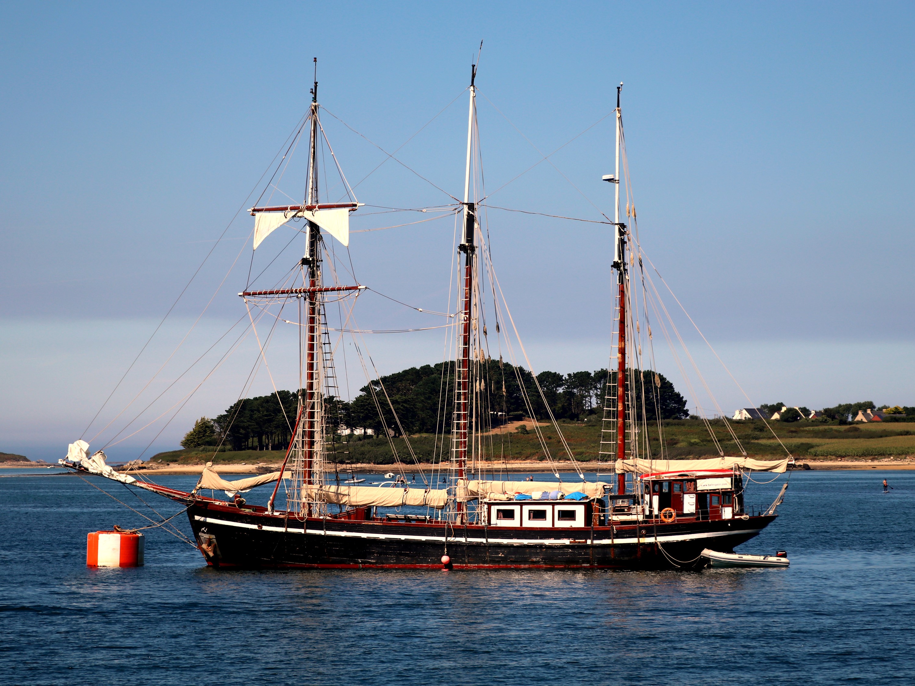 Sailing ship anchored in a bay with trees and houses on the shore HD Wallpaper