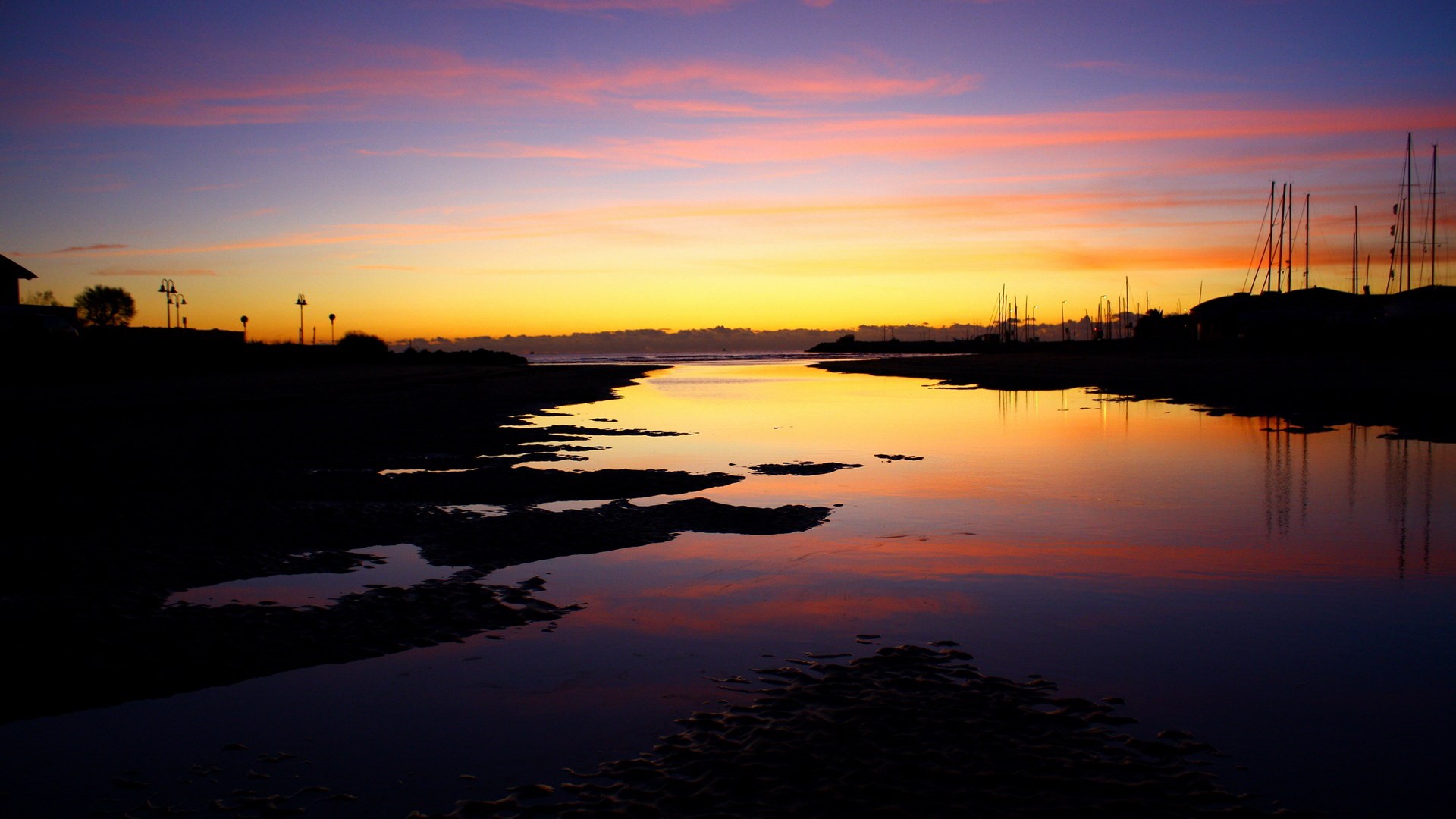 Sunset over a calm body of water with silhouetted boats HD Wallpaper