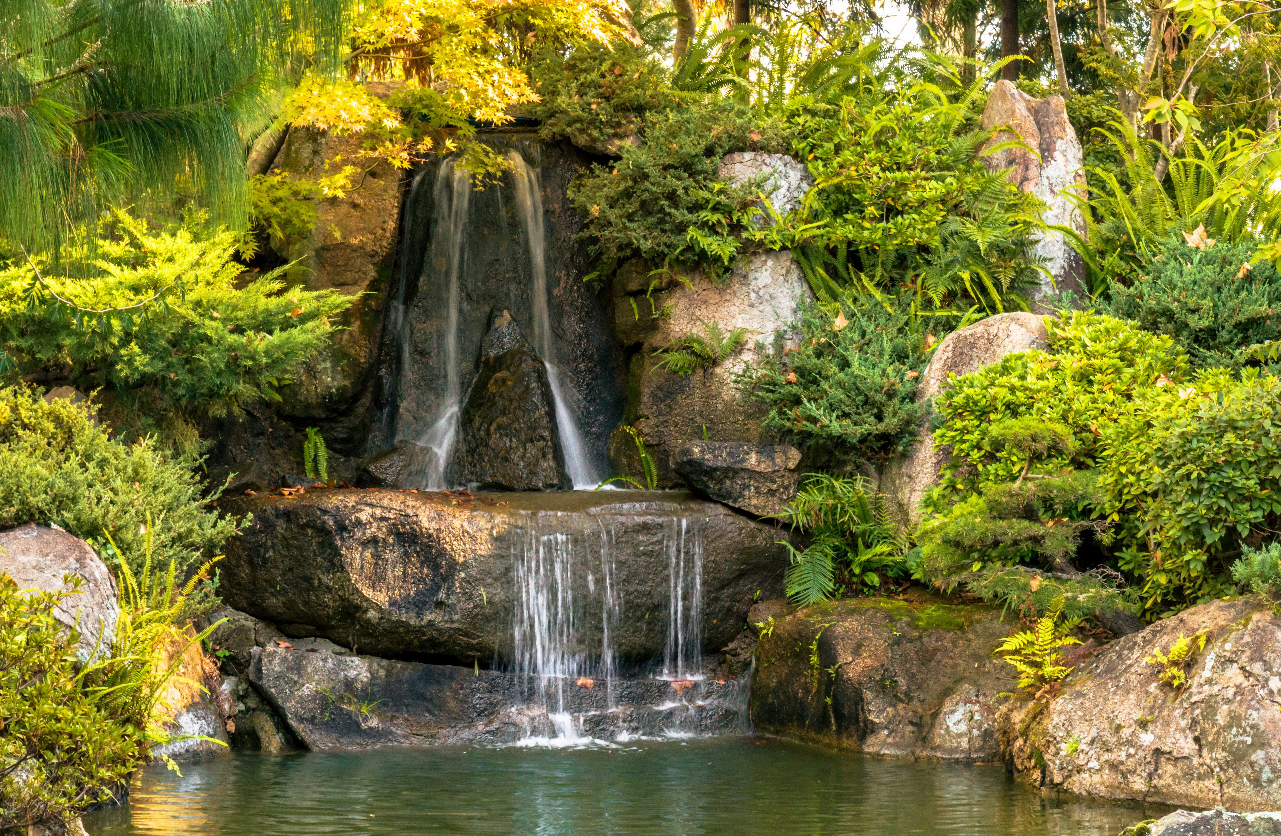 Waterfall cascading over rocks in a park HD Wallpaper