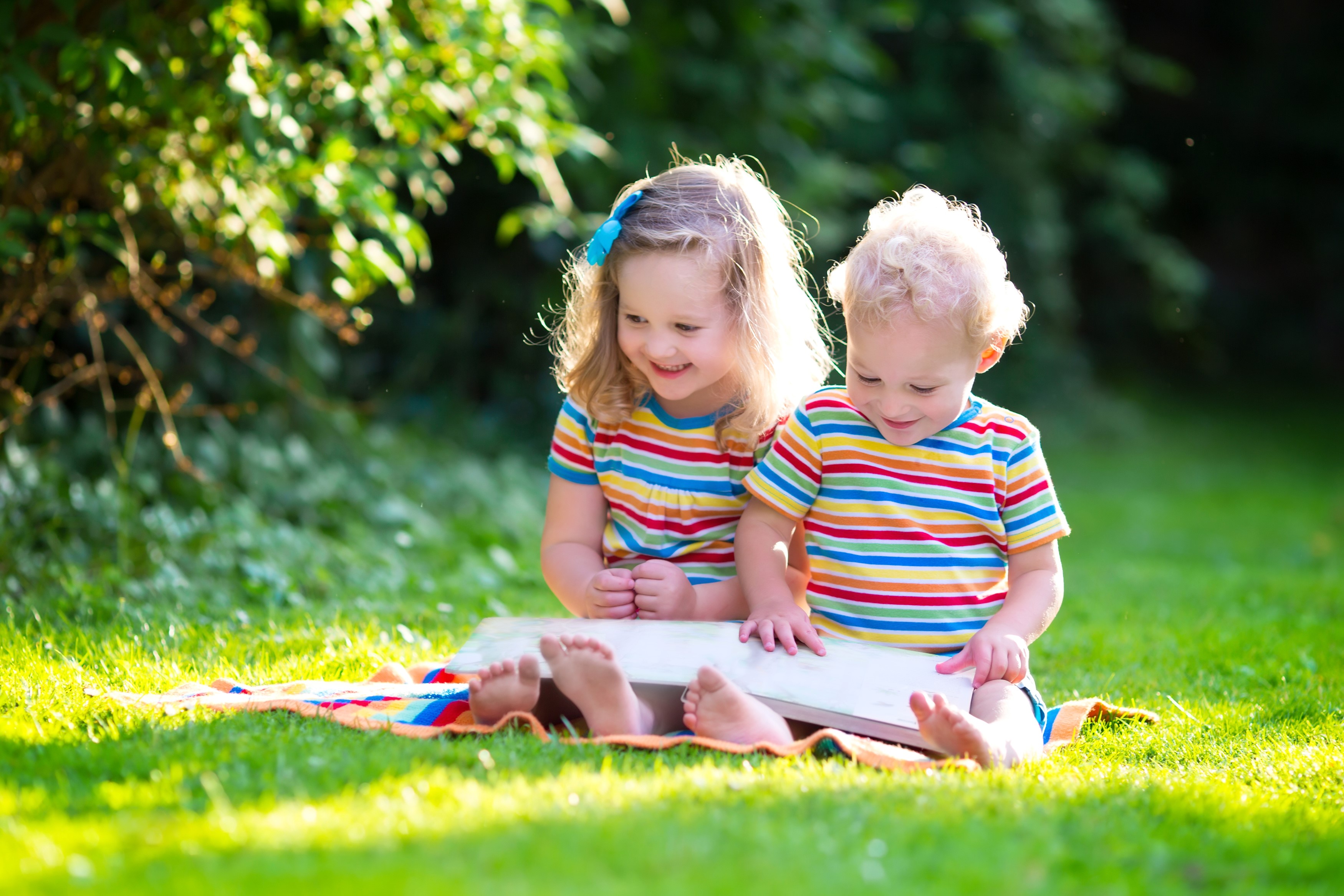 Two smiling children reading a book on a blanket HD Wallpaper