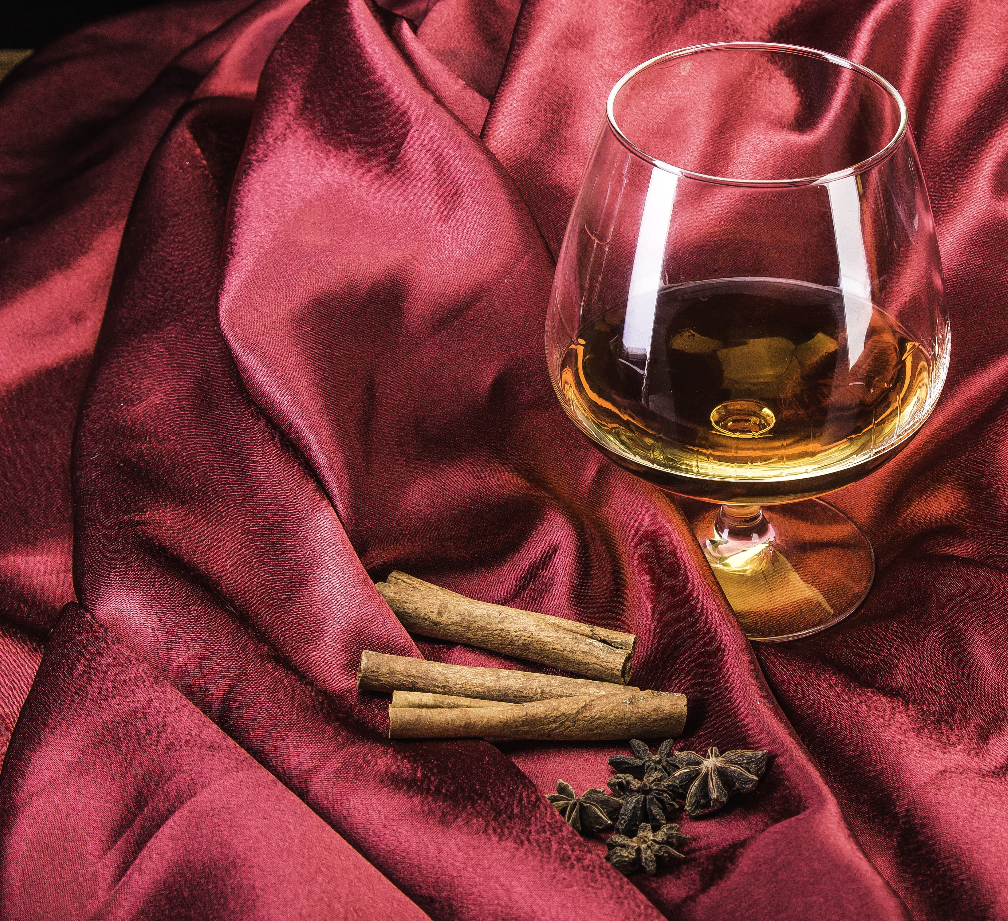Brandy glass with cinnamon and star anise on satin HD Wallpaper