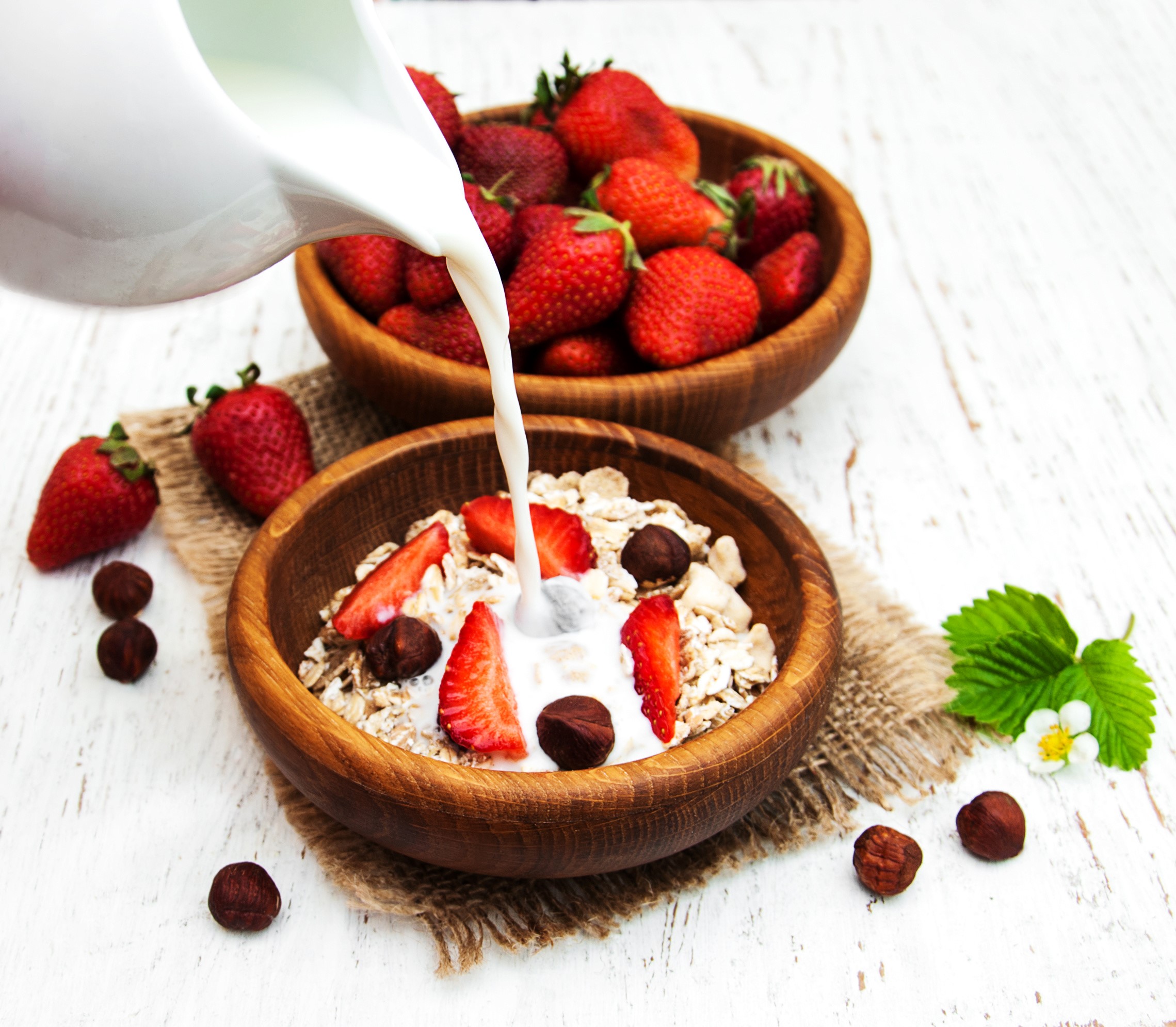 Milk being poured into a bowl of muesli with strawberries and hazelnuts HD Wallpaper