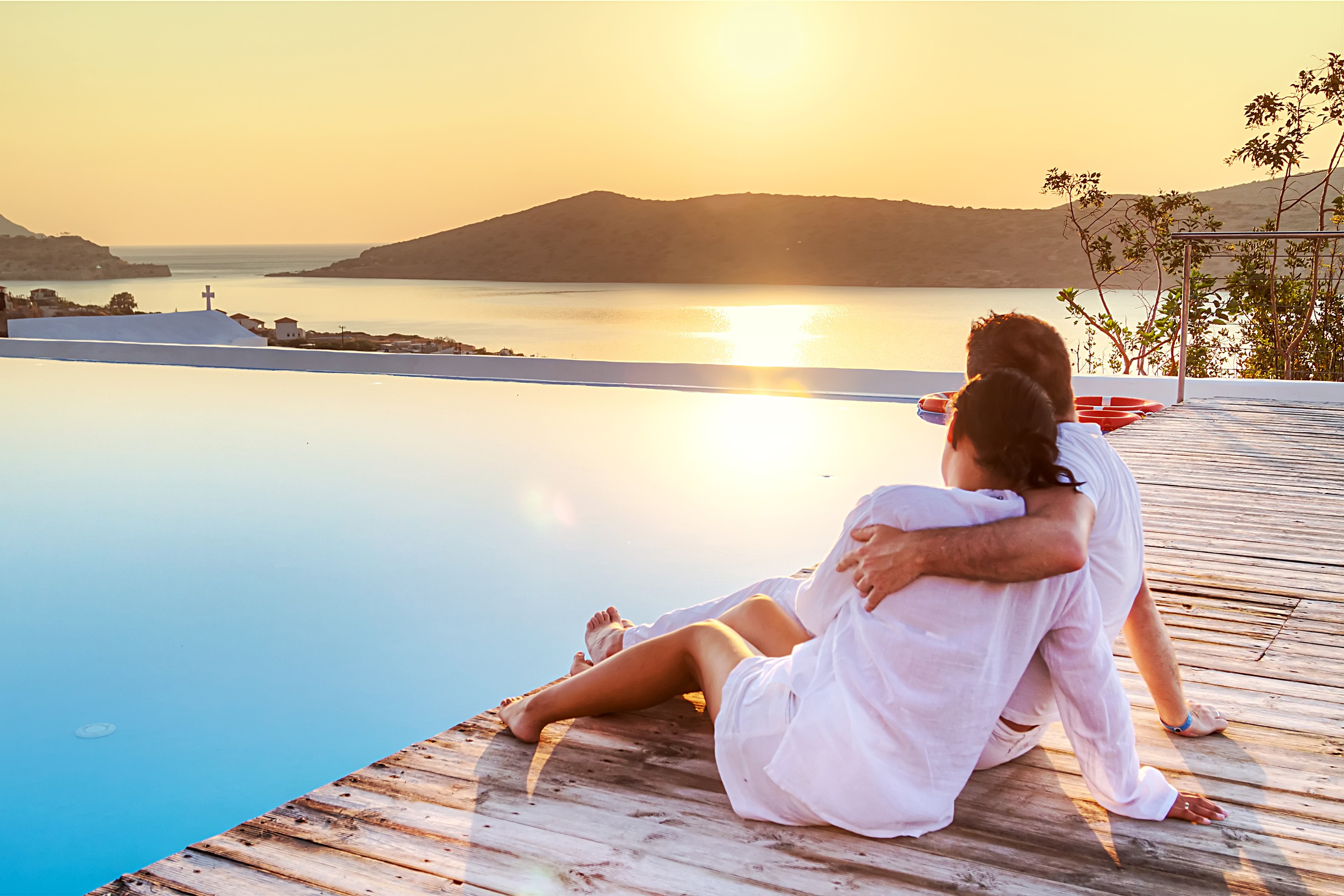 Couple embracing by infinity pool at sunset HD Wallpaper
