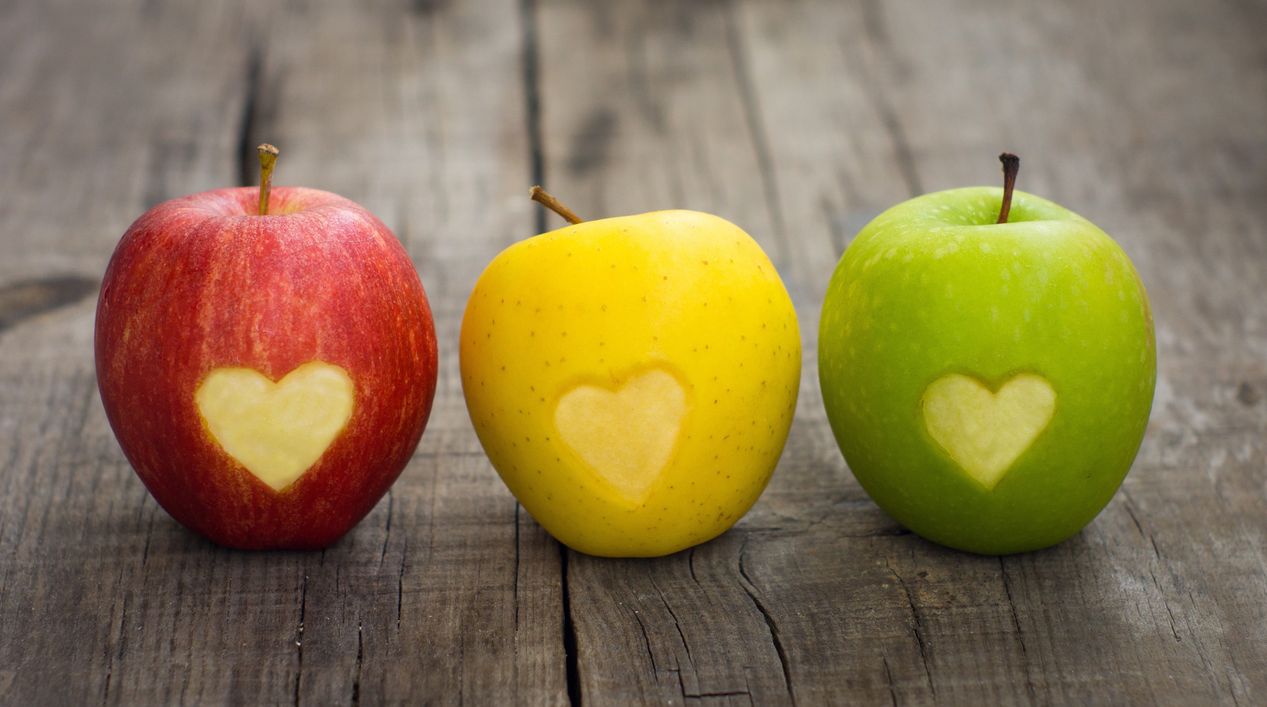 Three apples with carved hearts on wood planks HD Wallpaper