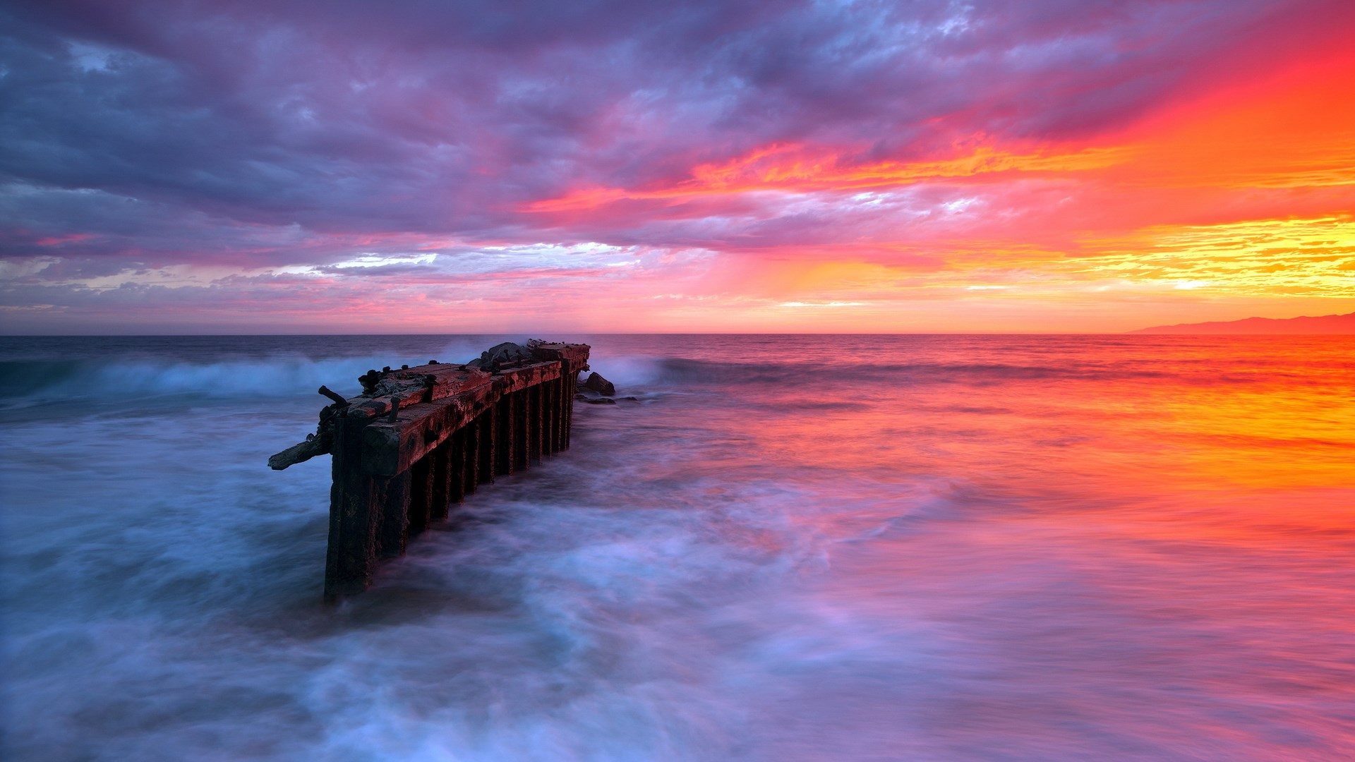 Ruined pier at sunset with colorful sky and ocean waves HD Wallpaper