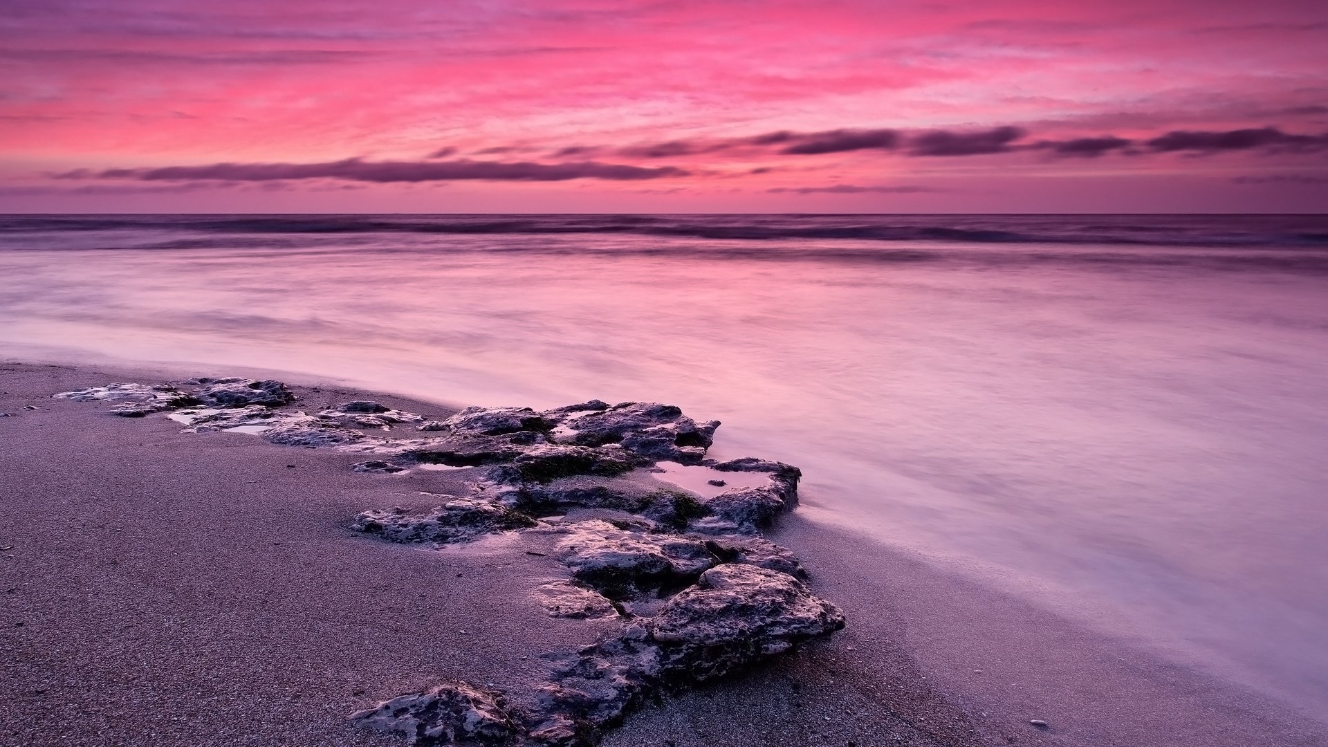 Pink sunset over a rocky beach with ocean waves HD Wallpaper