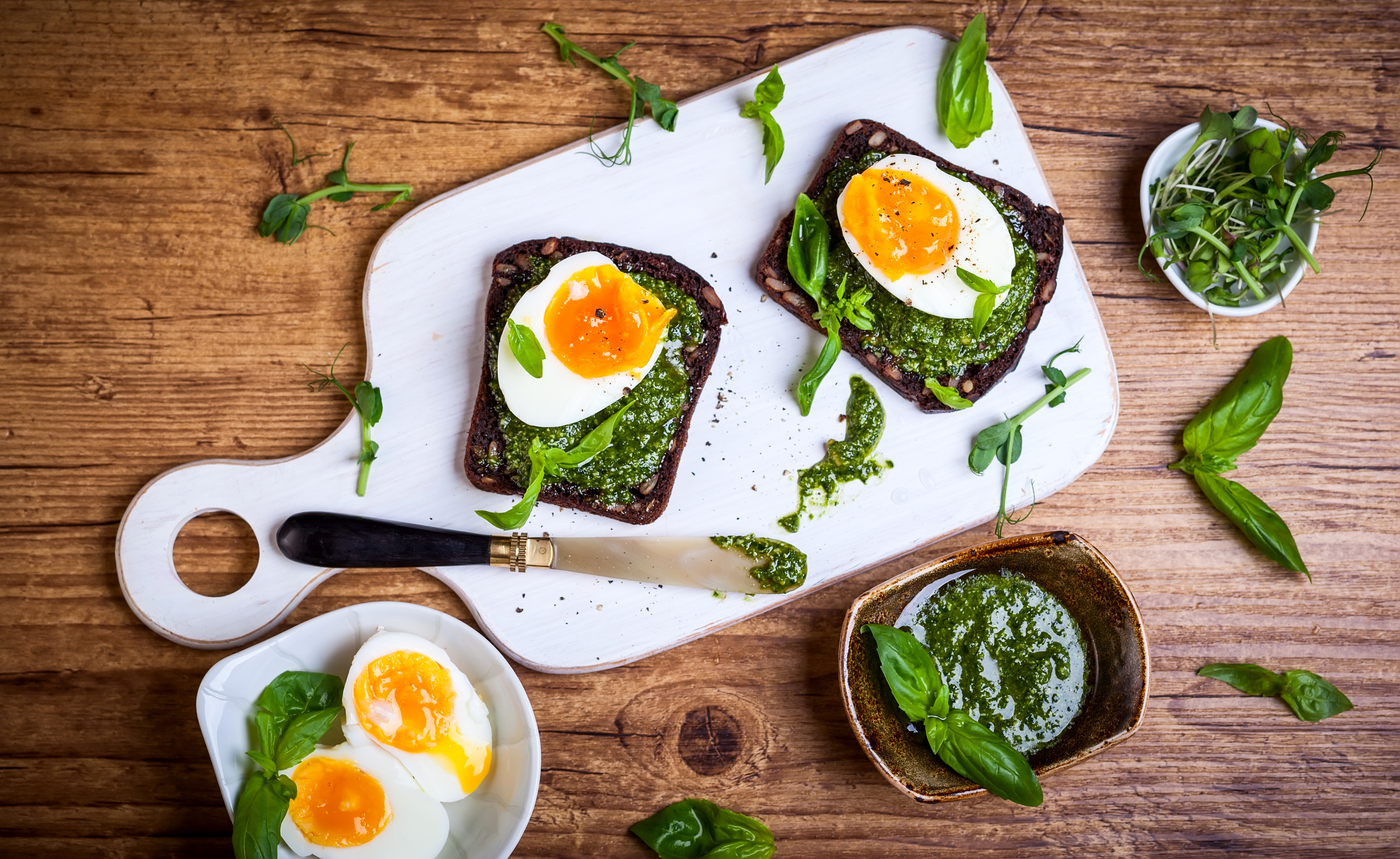 Two open-faced sandwiches with boiled eggs and pesto on a cutting board HD Wallpaper