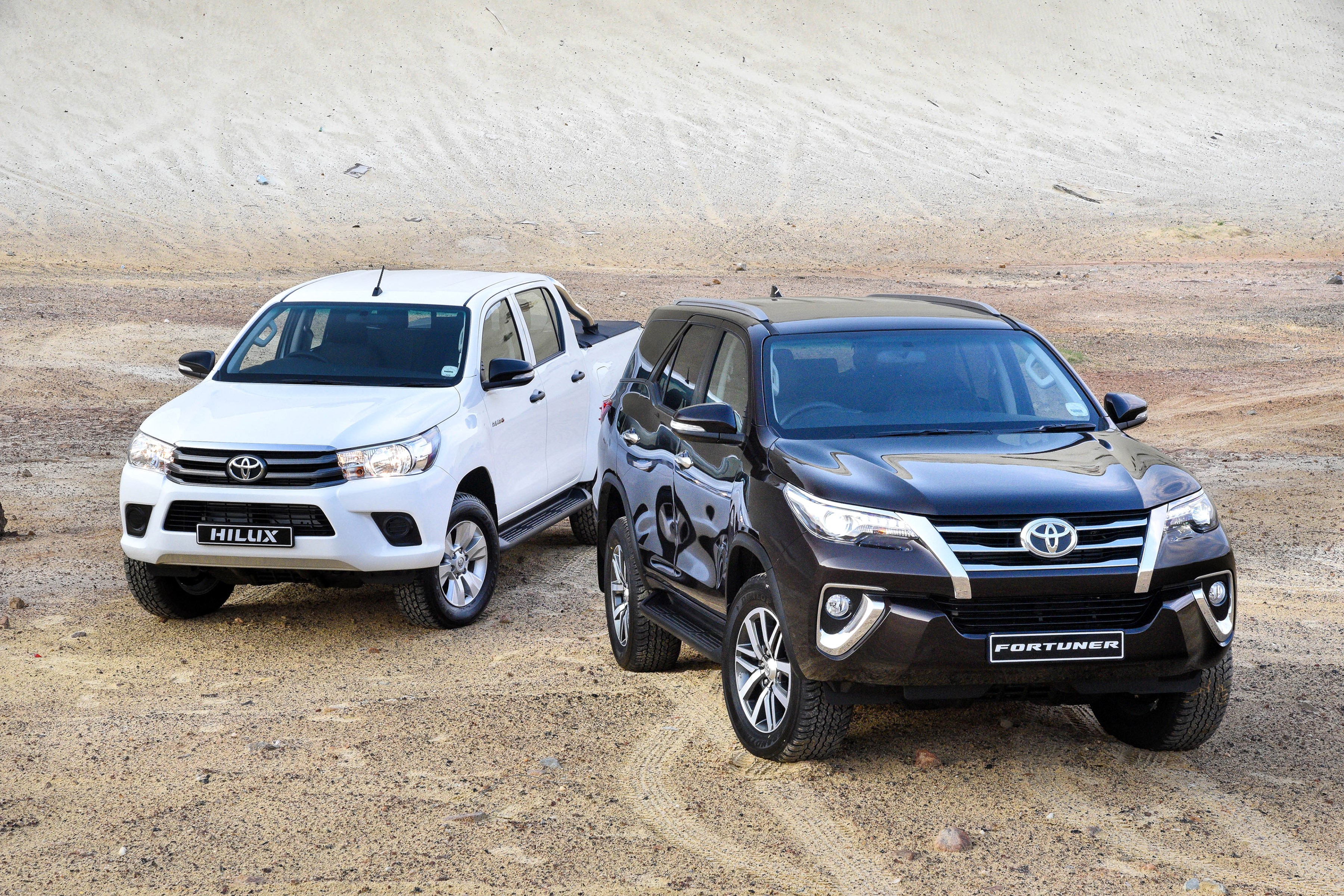 Two Toyota vehicles: a white Hilux and a dark Fortuner HD Wallpaper