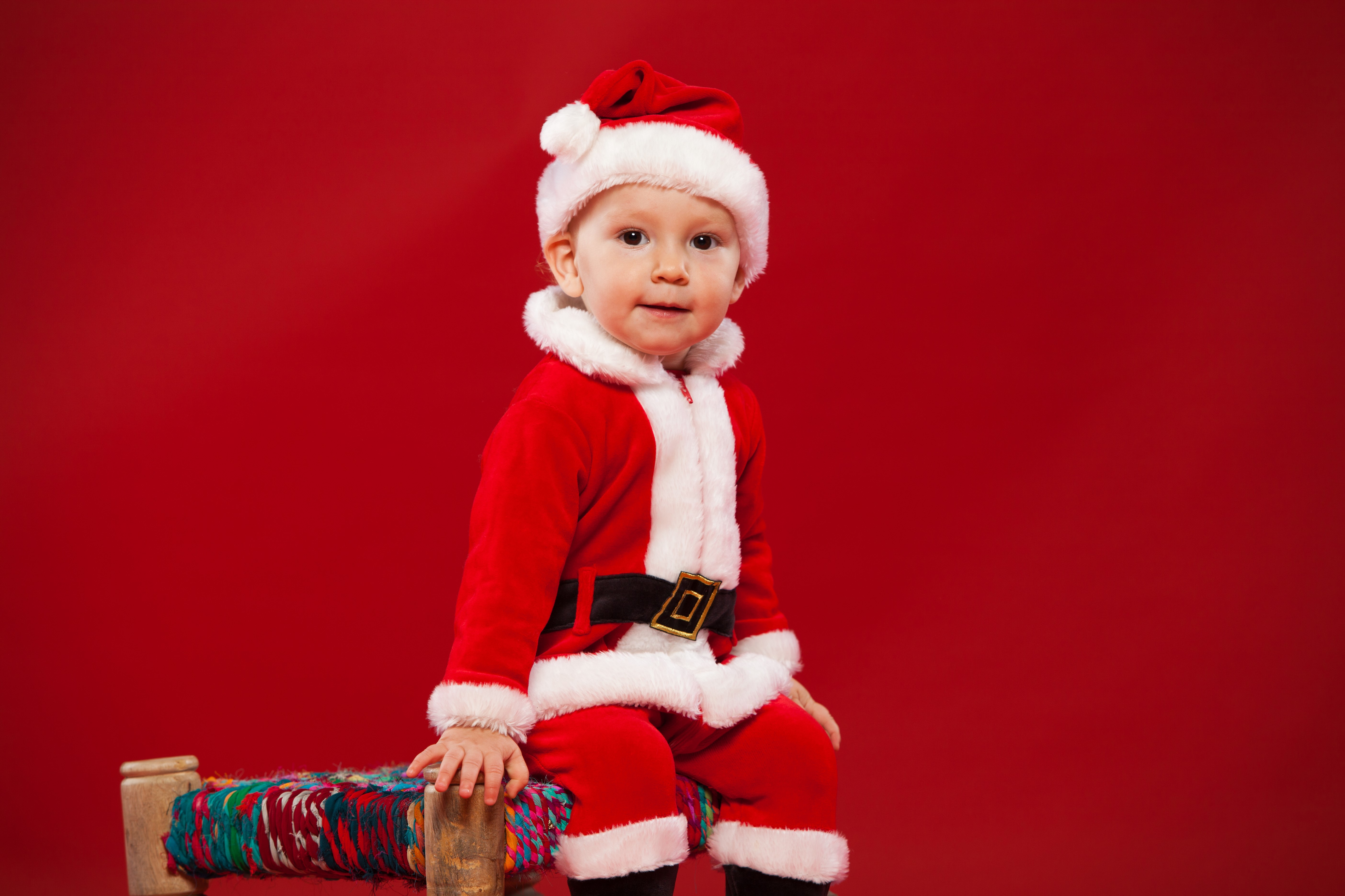 Boy in Santa Claus costume on red background HD Wallpaper