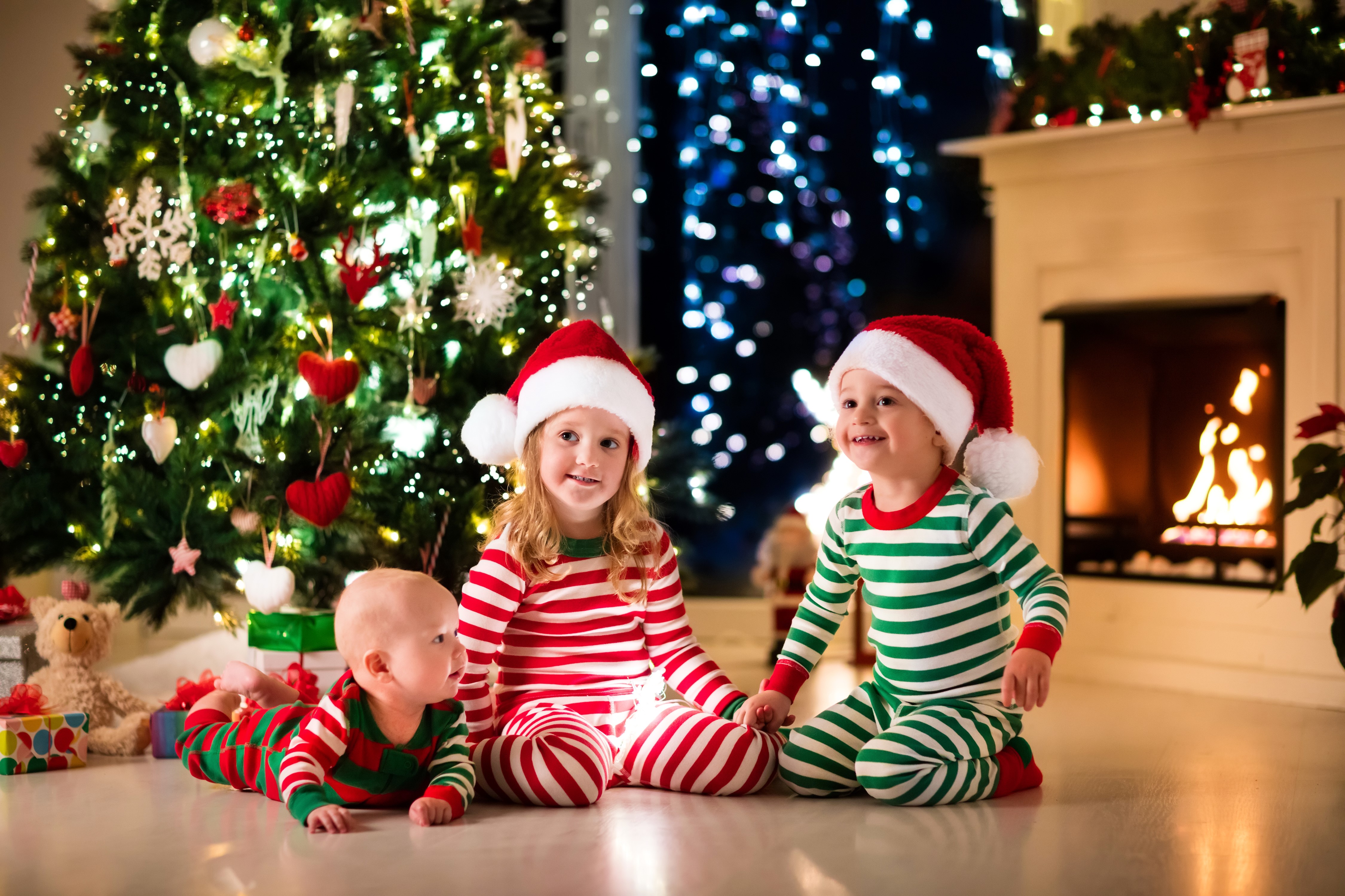 Three Children in Christmas Pajamas by Tree and Fireplace HD Wallpaper