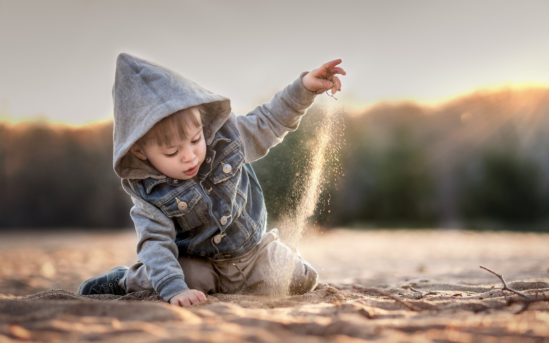 Boy in hooded jacket playing with sand on a beach HD Wallpaper