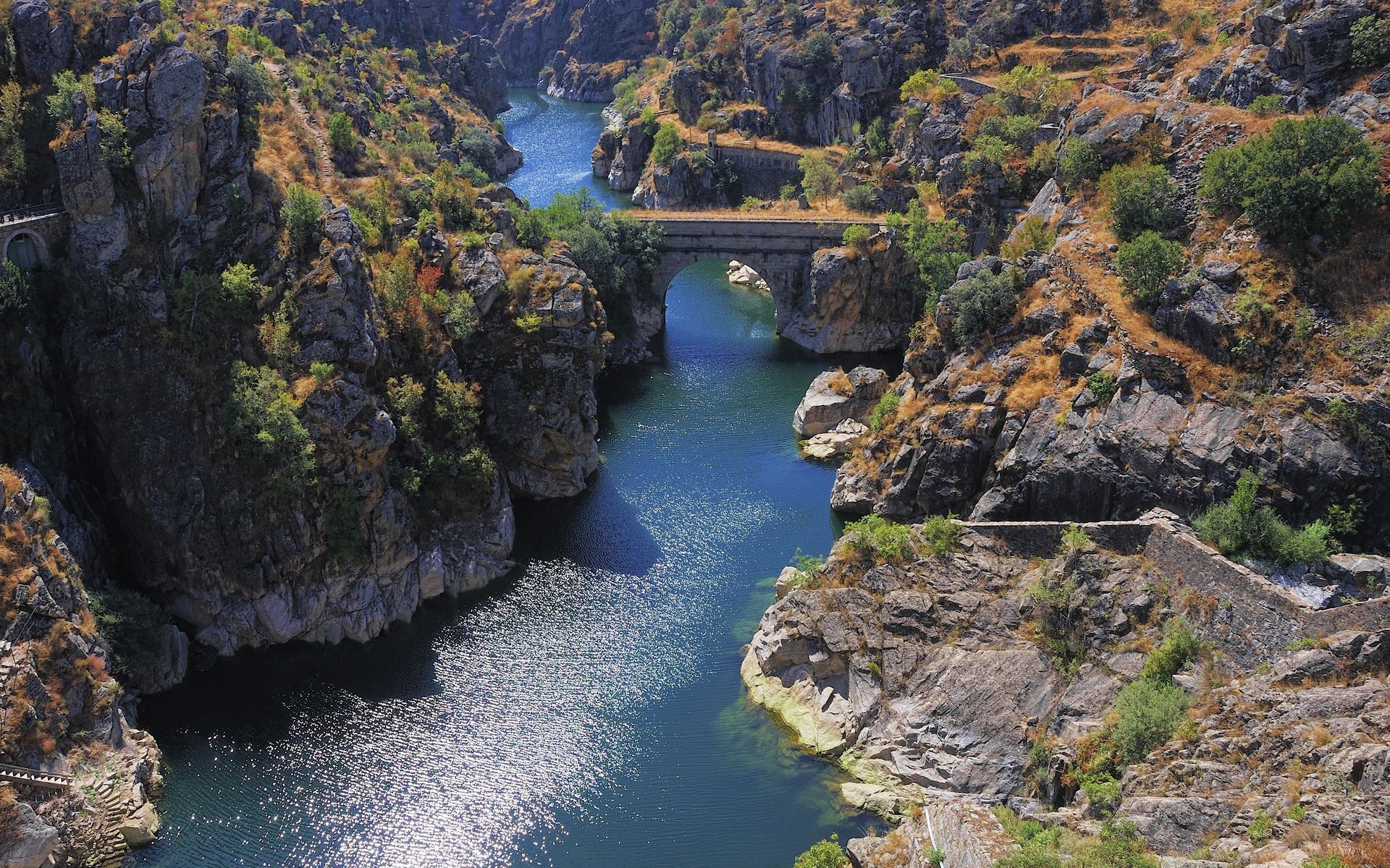 River flowing through a rocky gorge with a stone bridge HD Wallpaper