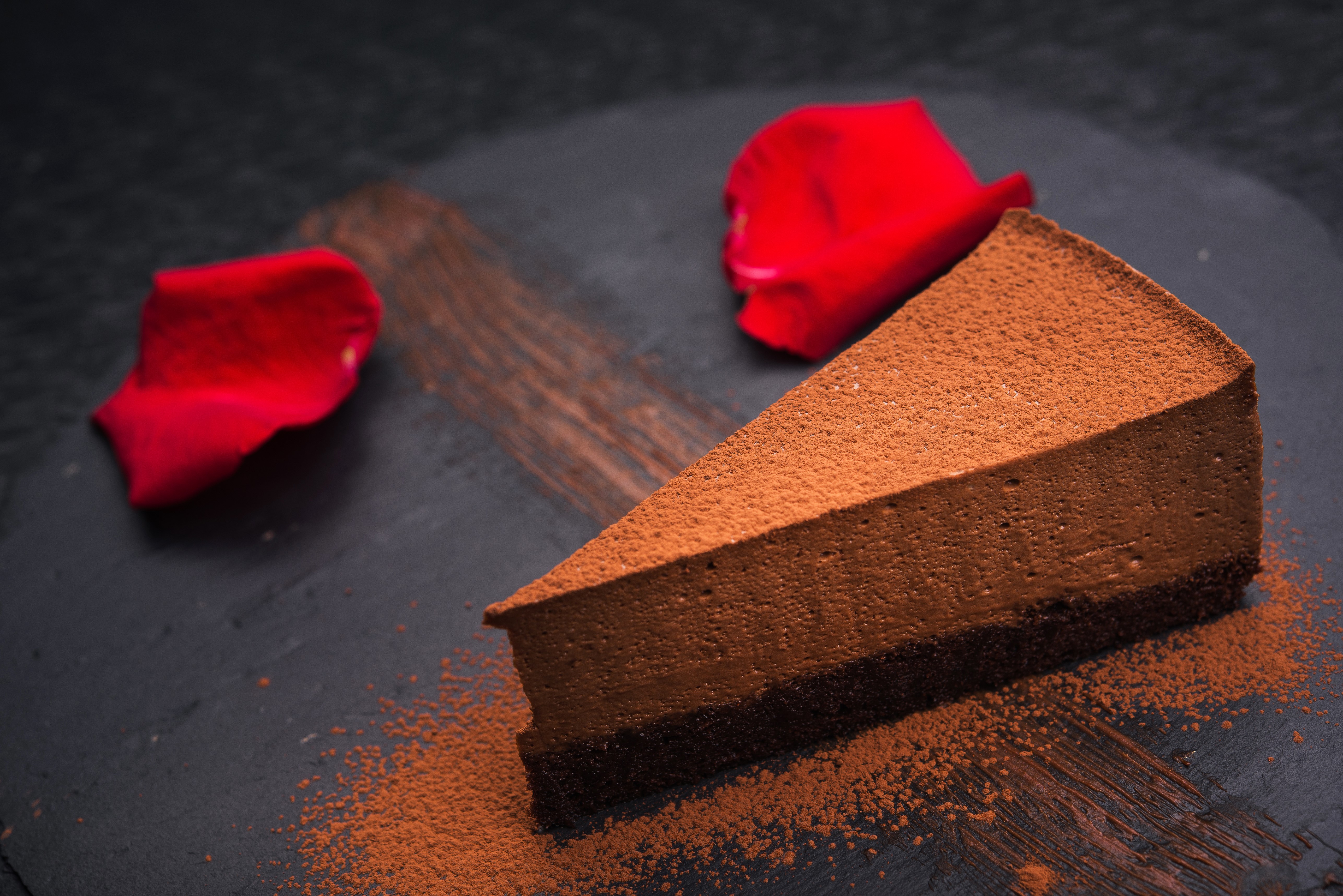 Chocolate cake slice with cocoa powder and rose petals HD Wallpaper