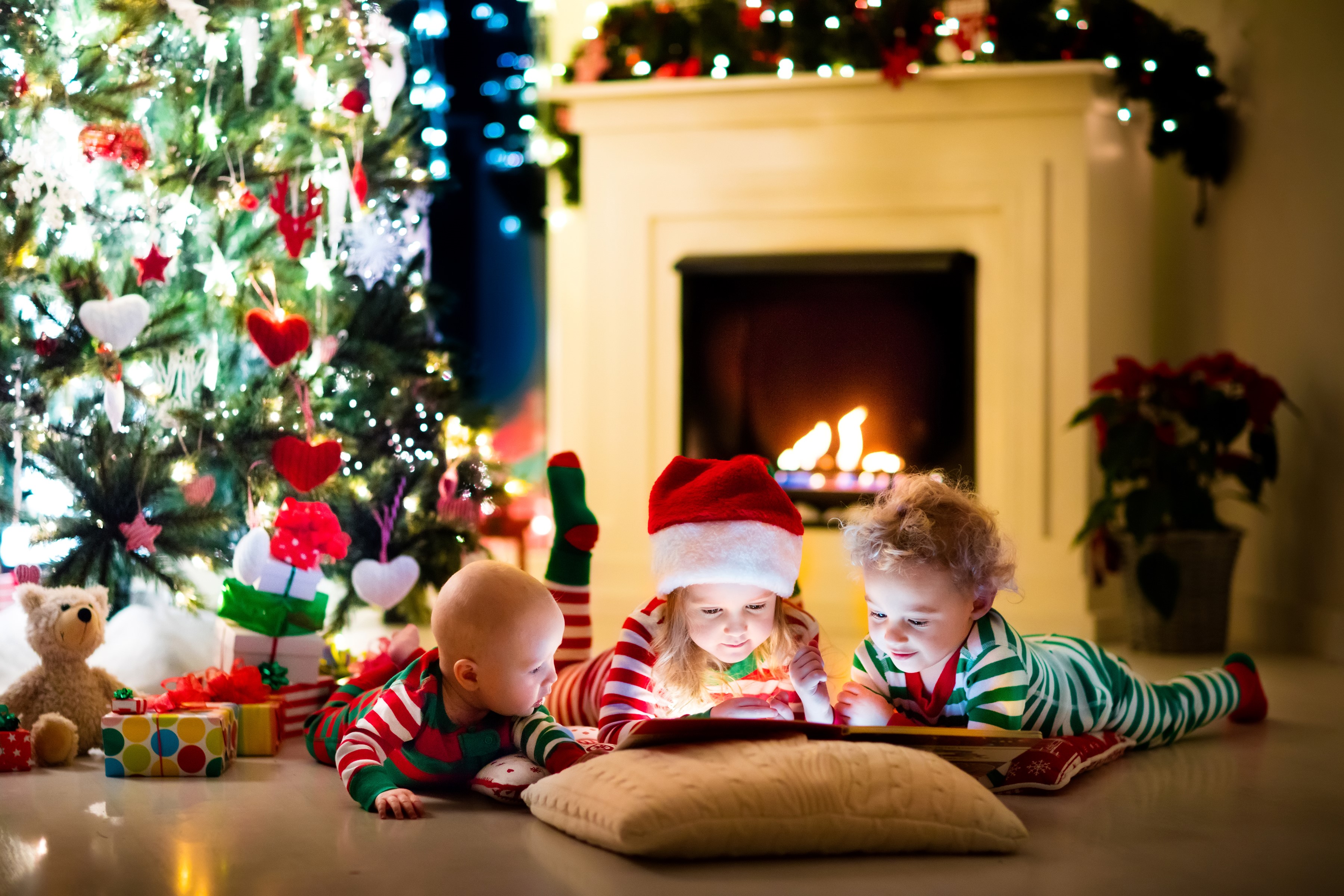 Three children reading a book by the fireplace and Christmas tree HD Wallpaper