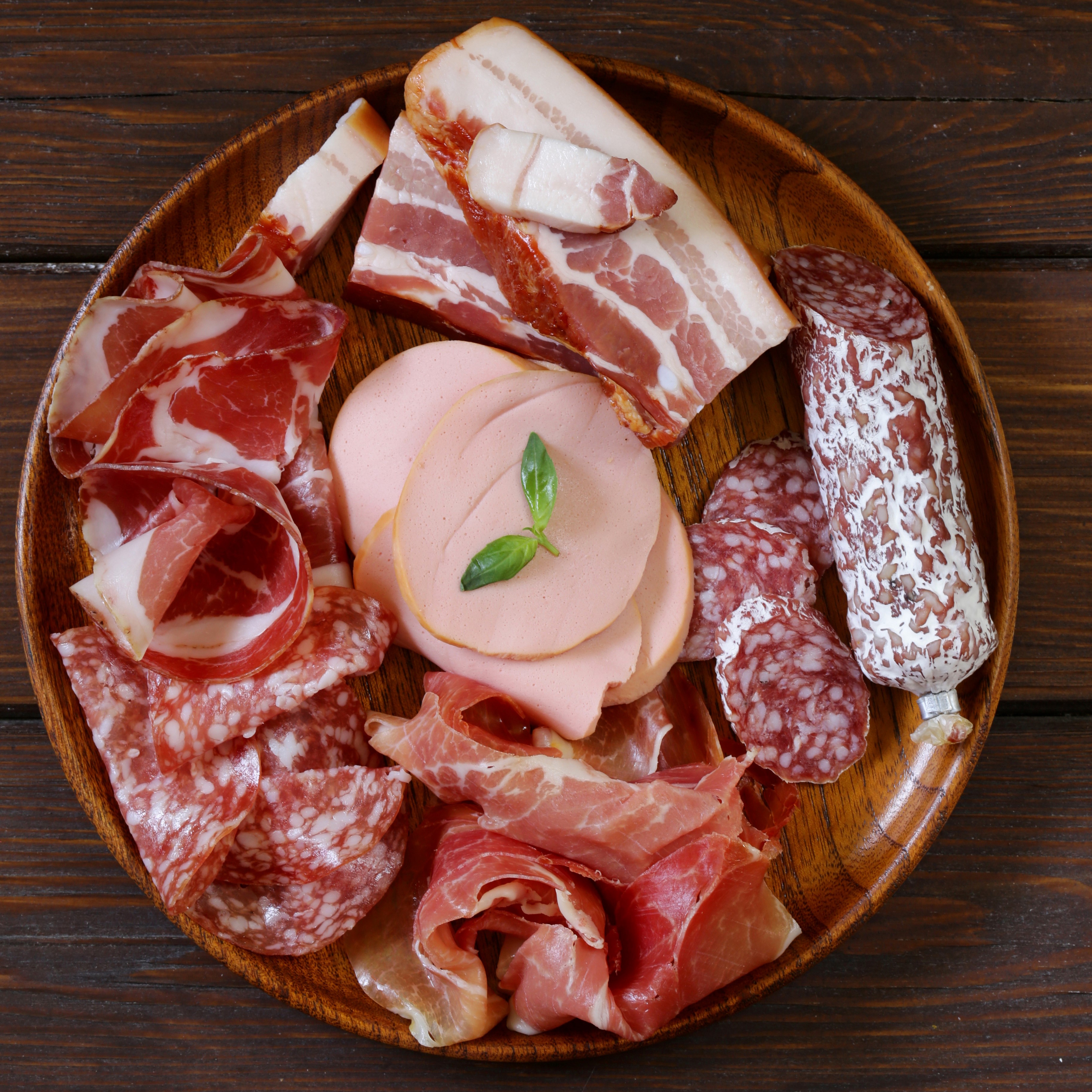 Assortment of cured meats and sausages on a wooden plate HD Wallpaper