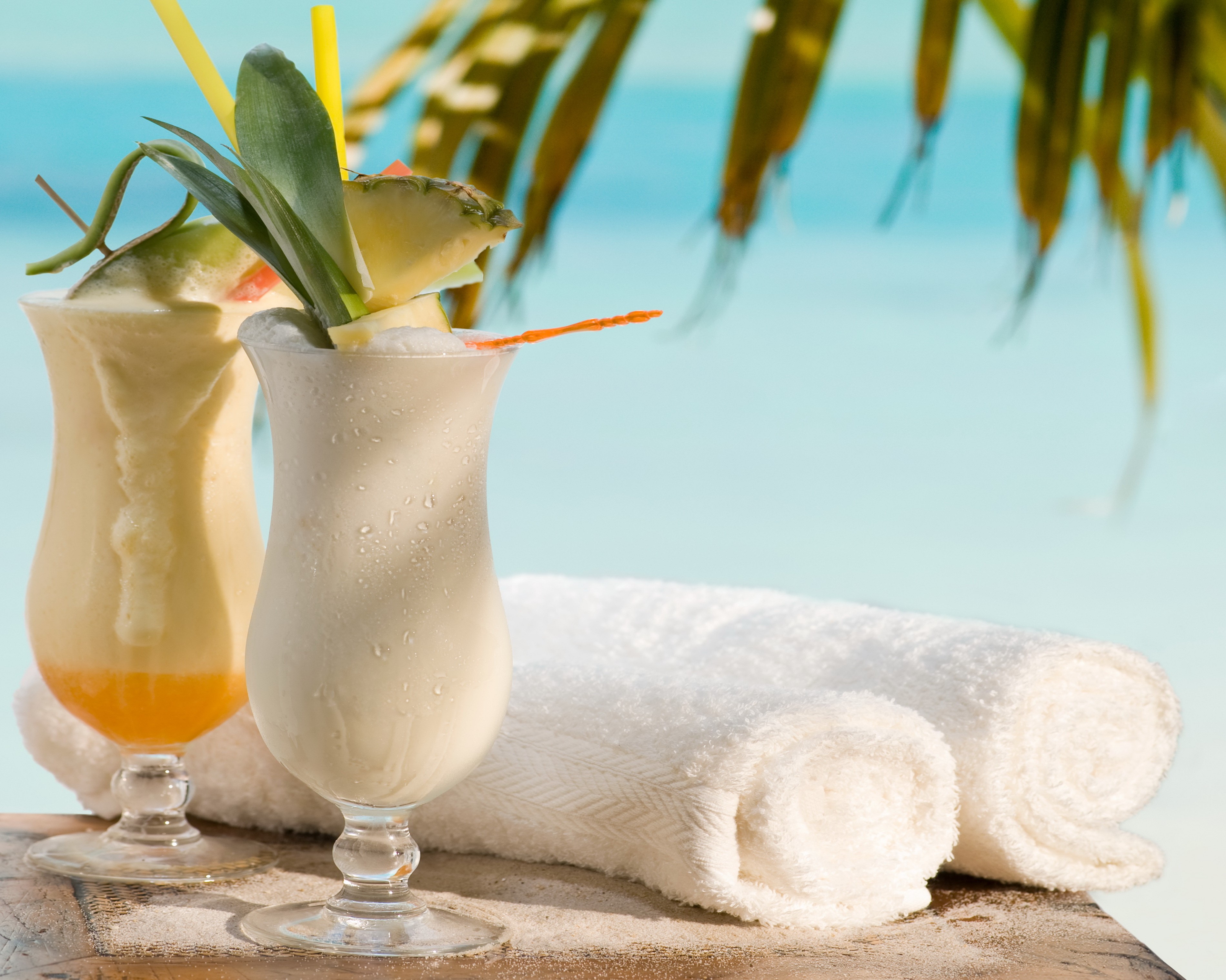 Two tropical cocktails with pineapple and towels on a beach HD Wallpaper