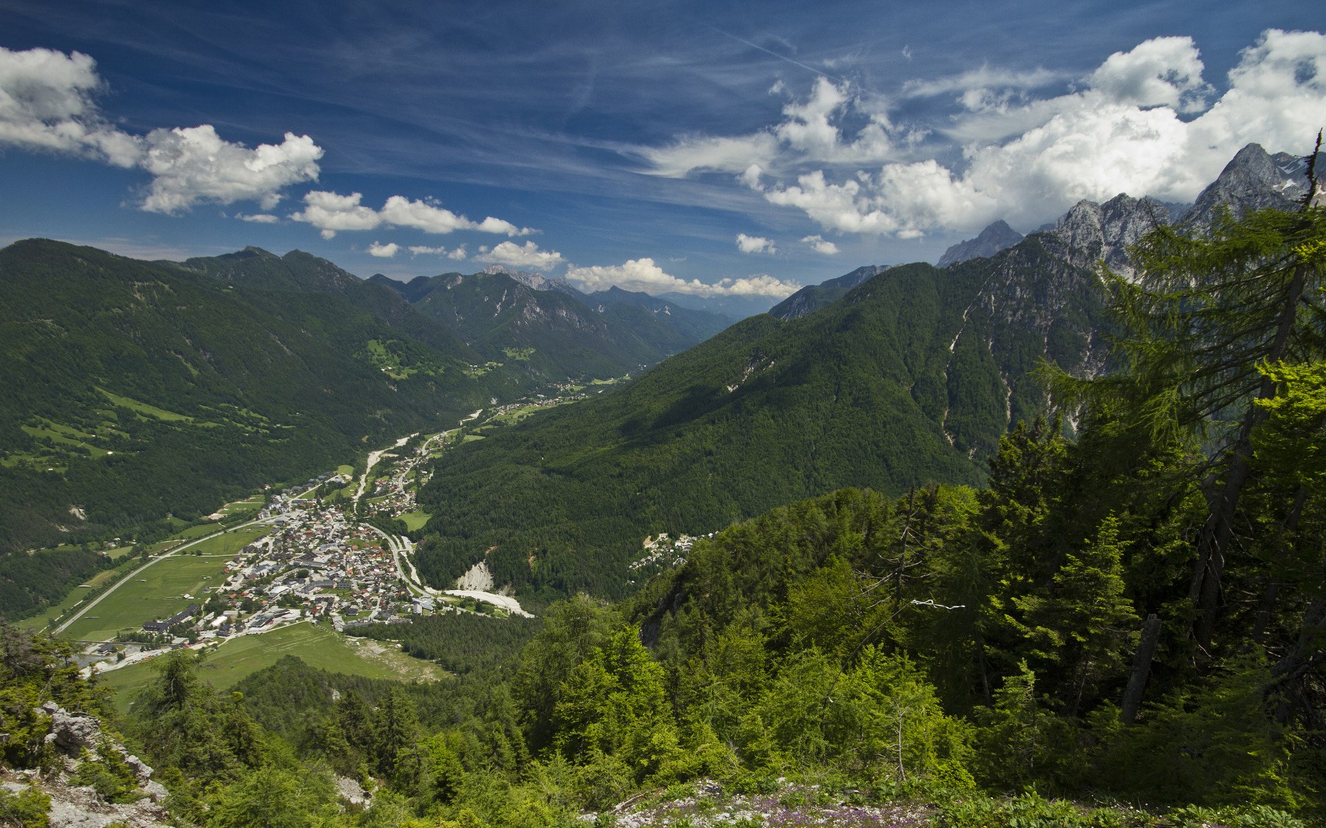 Mountain valley with a town and forested slopes HD Wallpaper