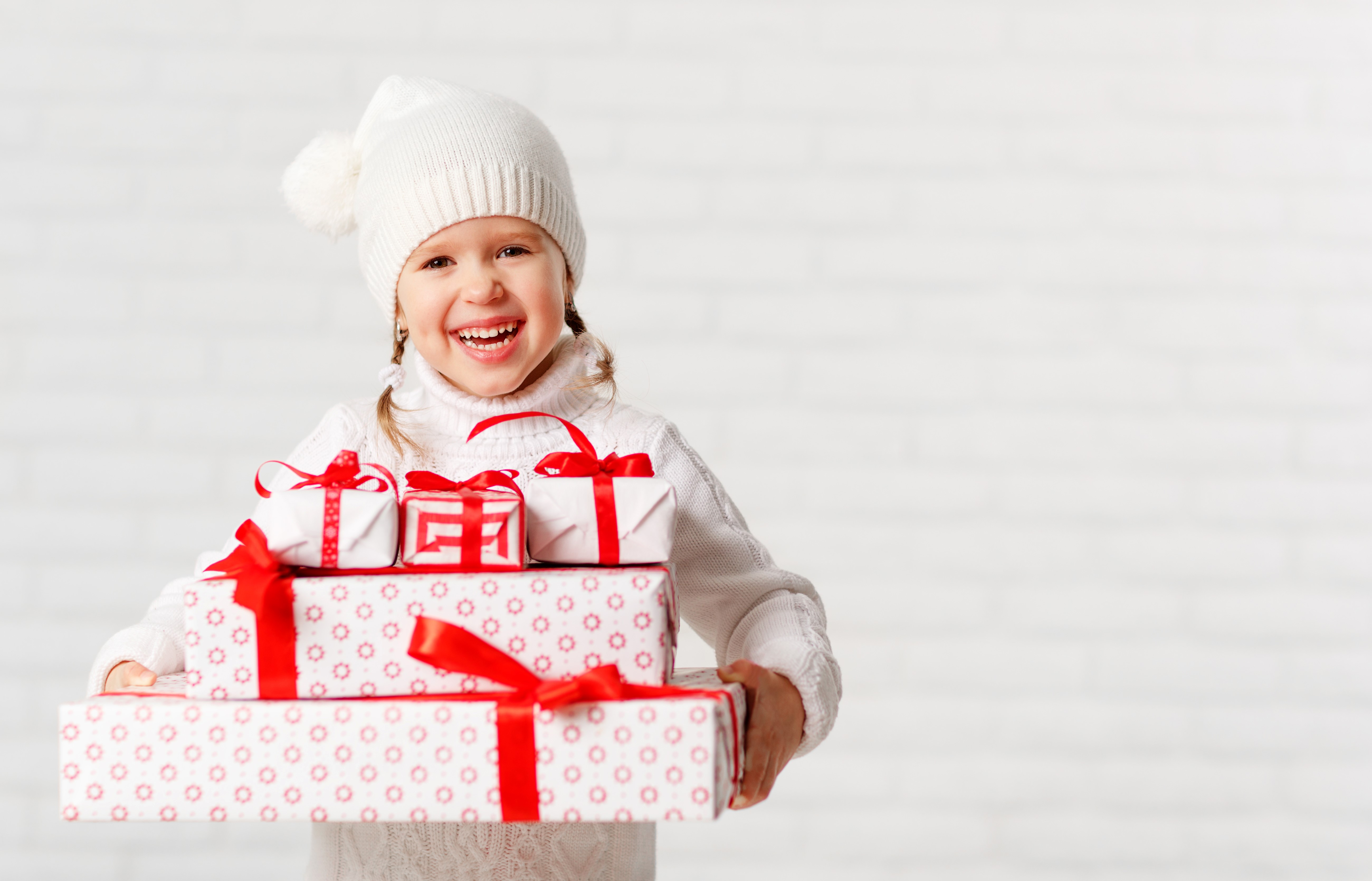 Little girl in winter hat holding Christmas gifts HD Wallpaper