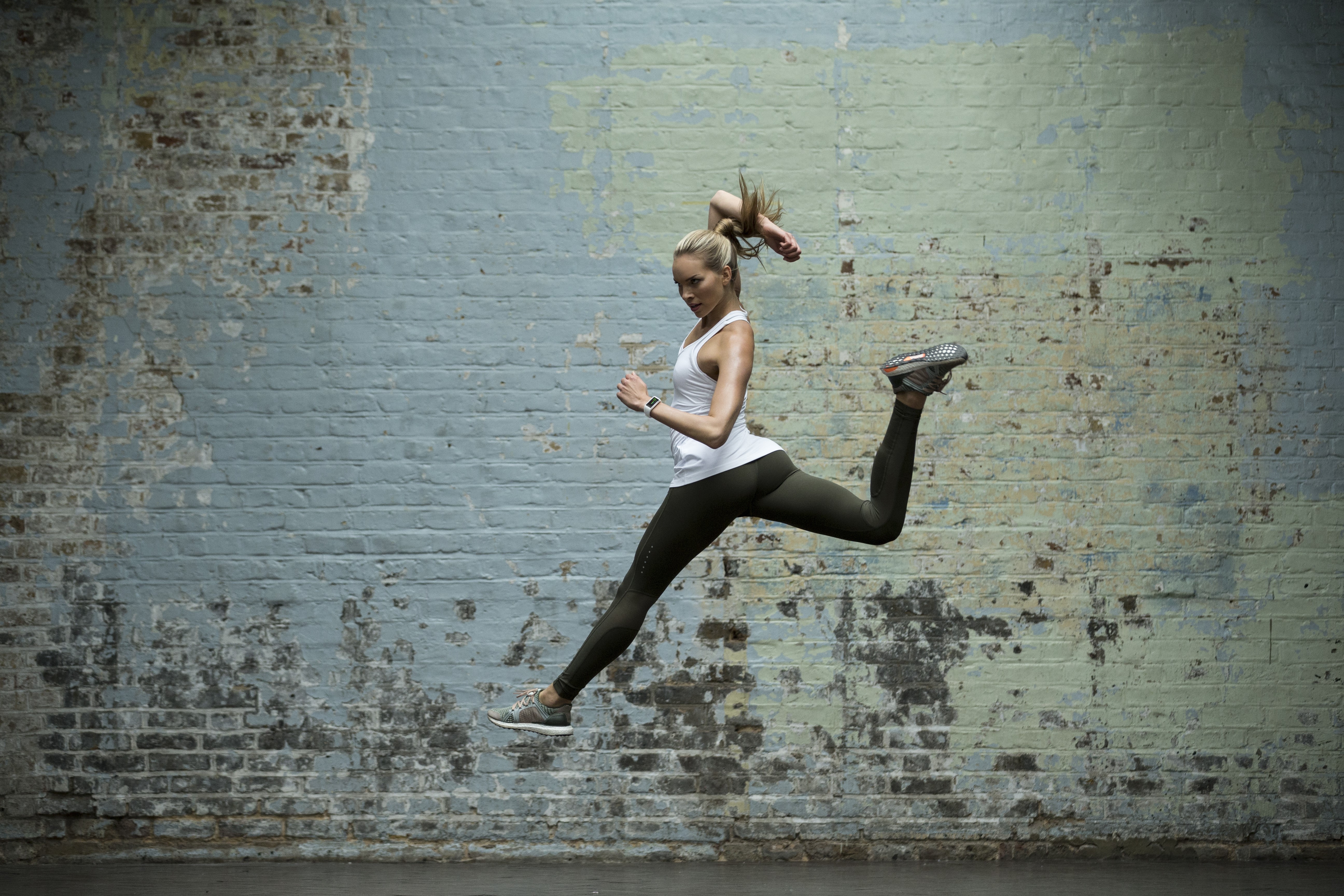 Woman jumping in front of a brick wall HD Wallpaper