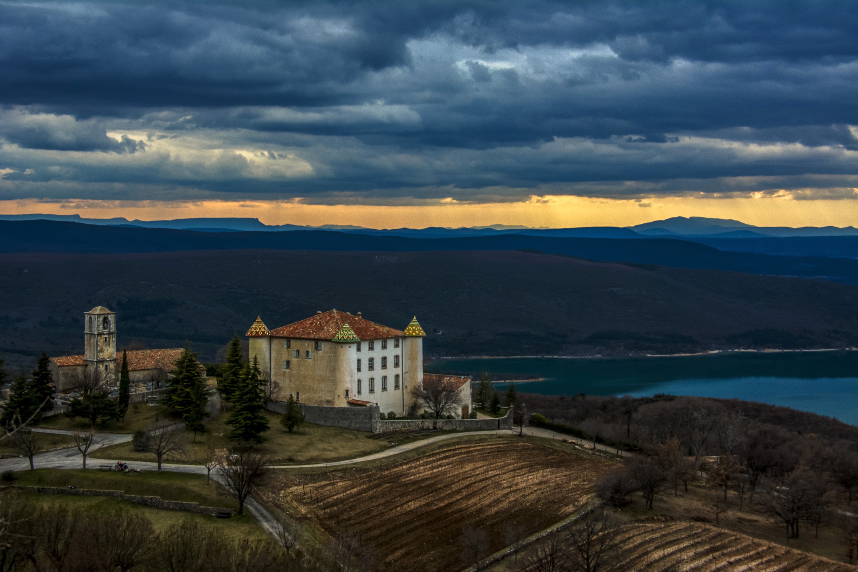 Chateau d'Aiguines and church overlooking a lake at sunset HD Wallpaper