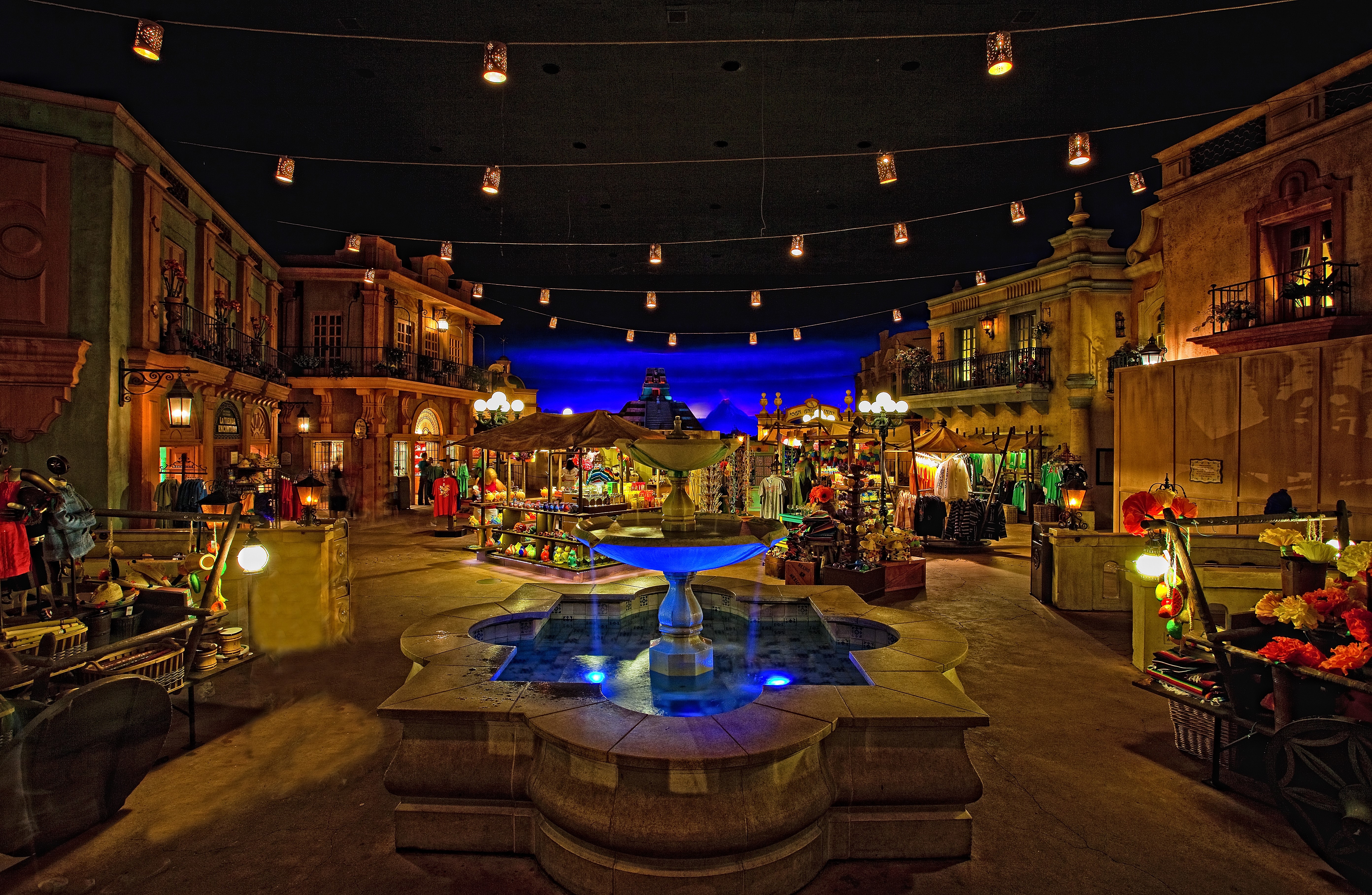 Nighttime street scene with fountain and shops HD Wallpaper