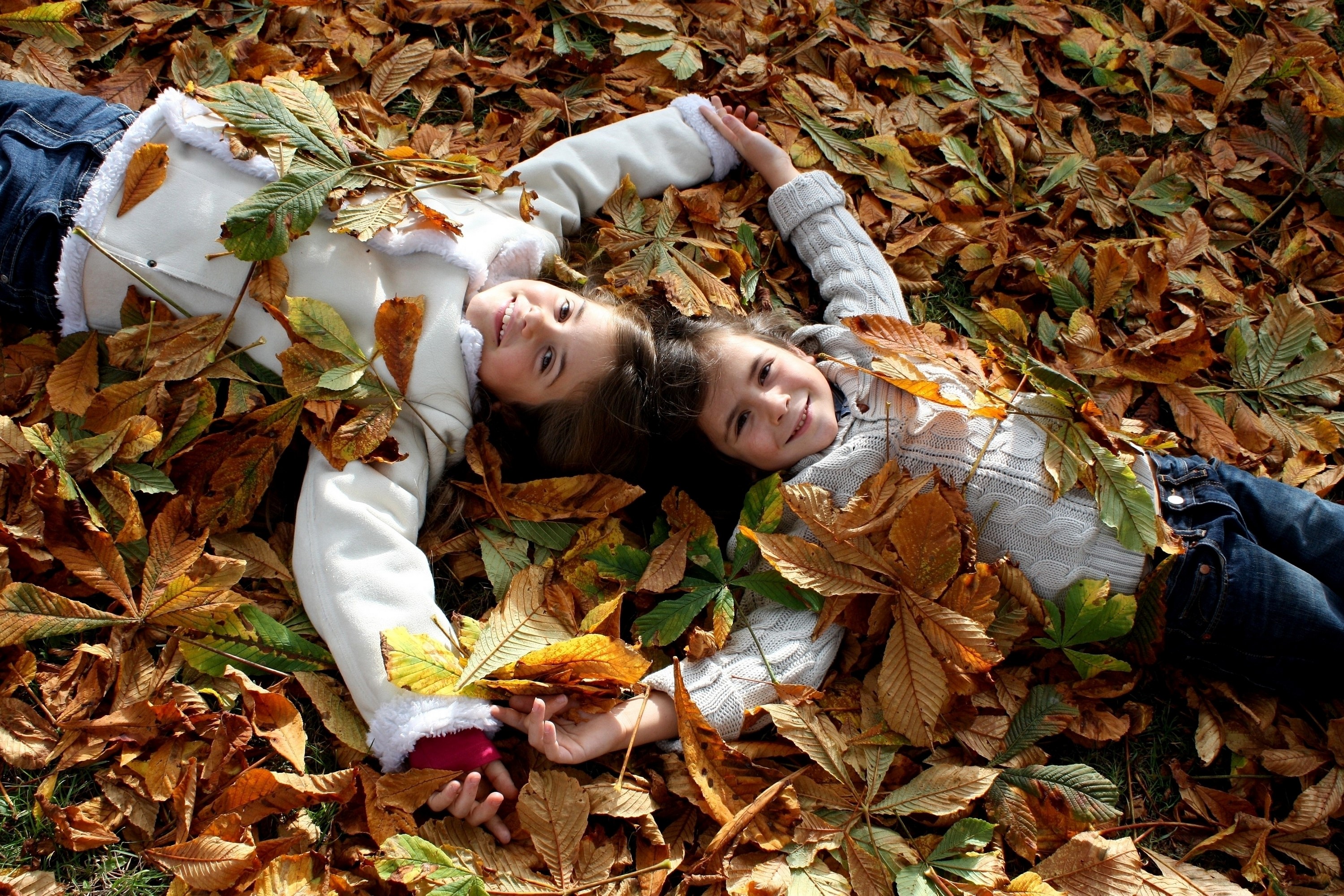 Two young girls lying in autumn foliage HD Wallpaper