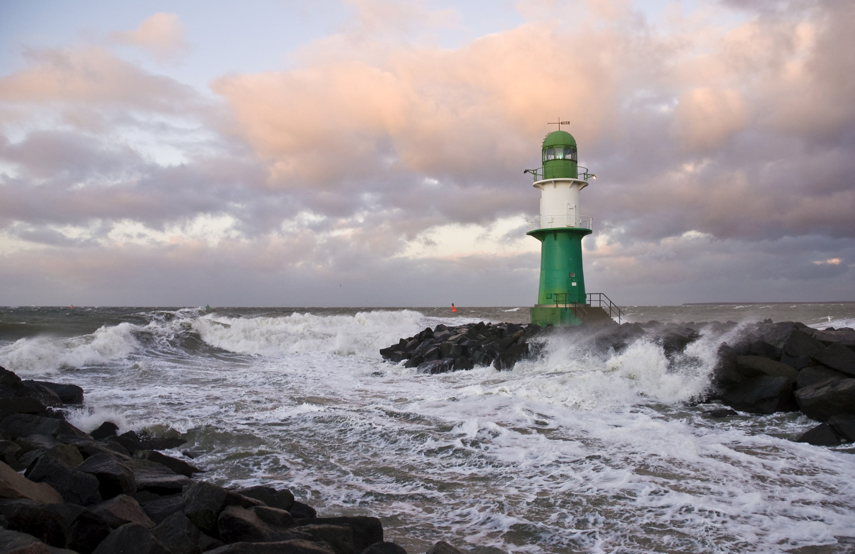 Green and white lighthouse on rocky shore with waves and clouds HD Wallpaper