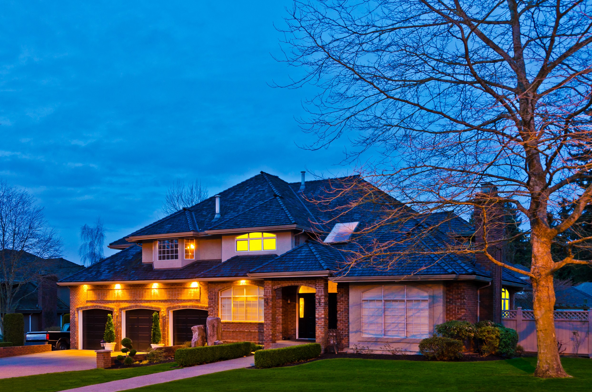 Luxury brick house with garage and trees at dusk HD Wallpaper