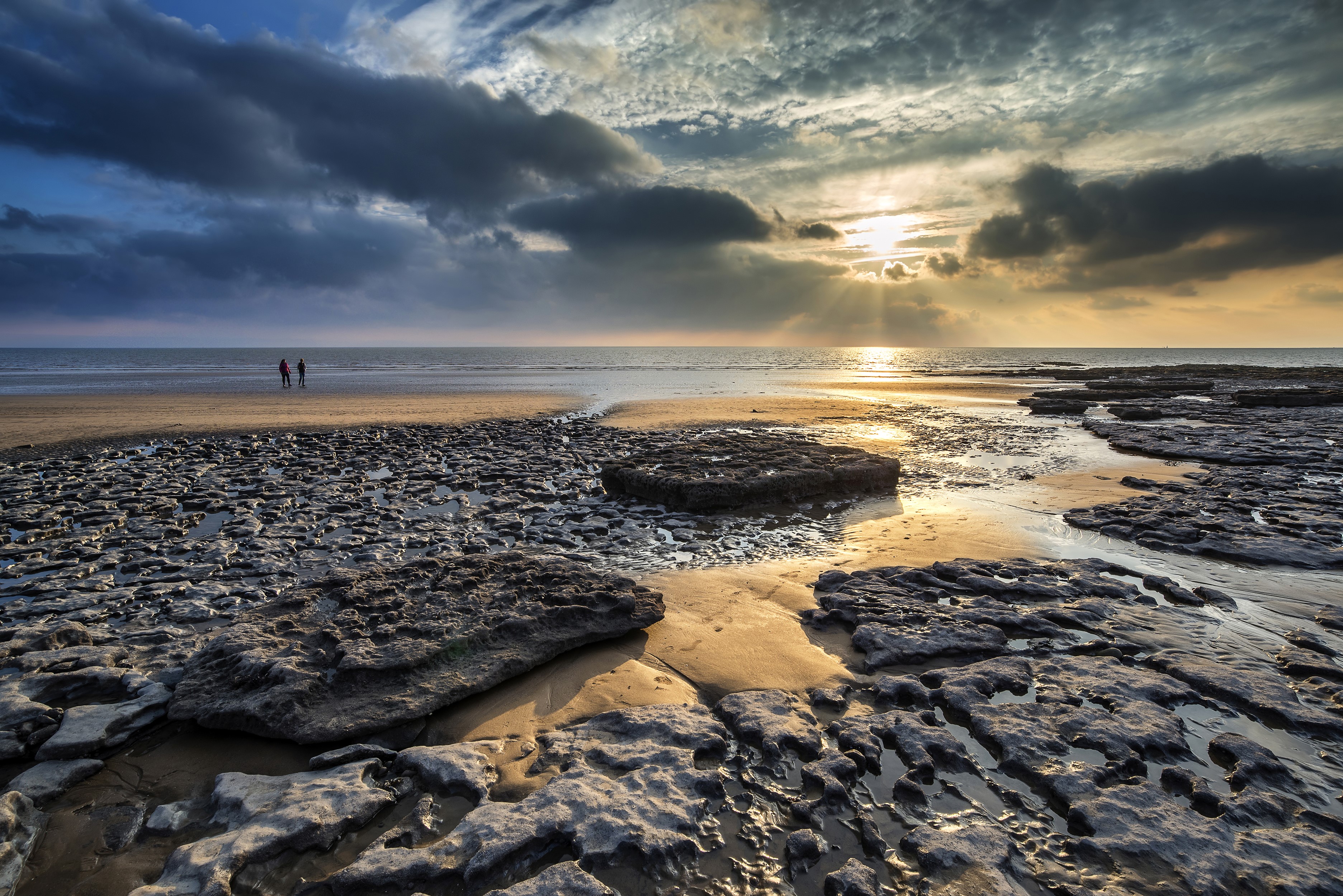 Dunraven Bay, Wales: Sunset over rocky beach with two people HD Wallpaper