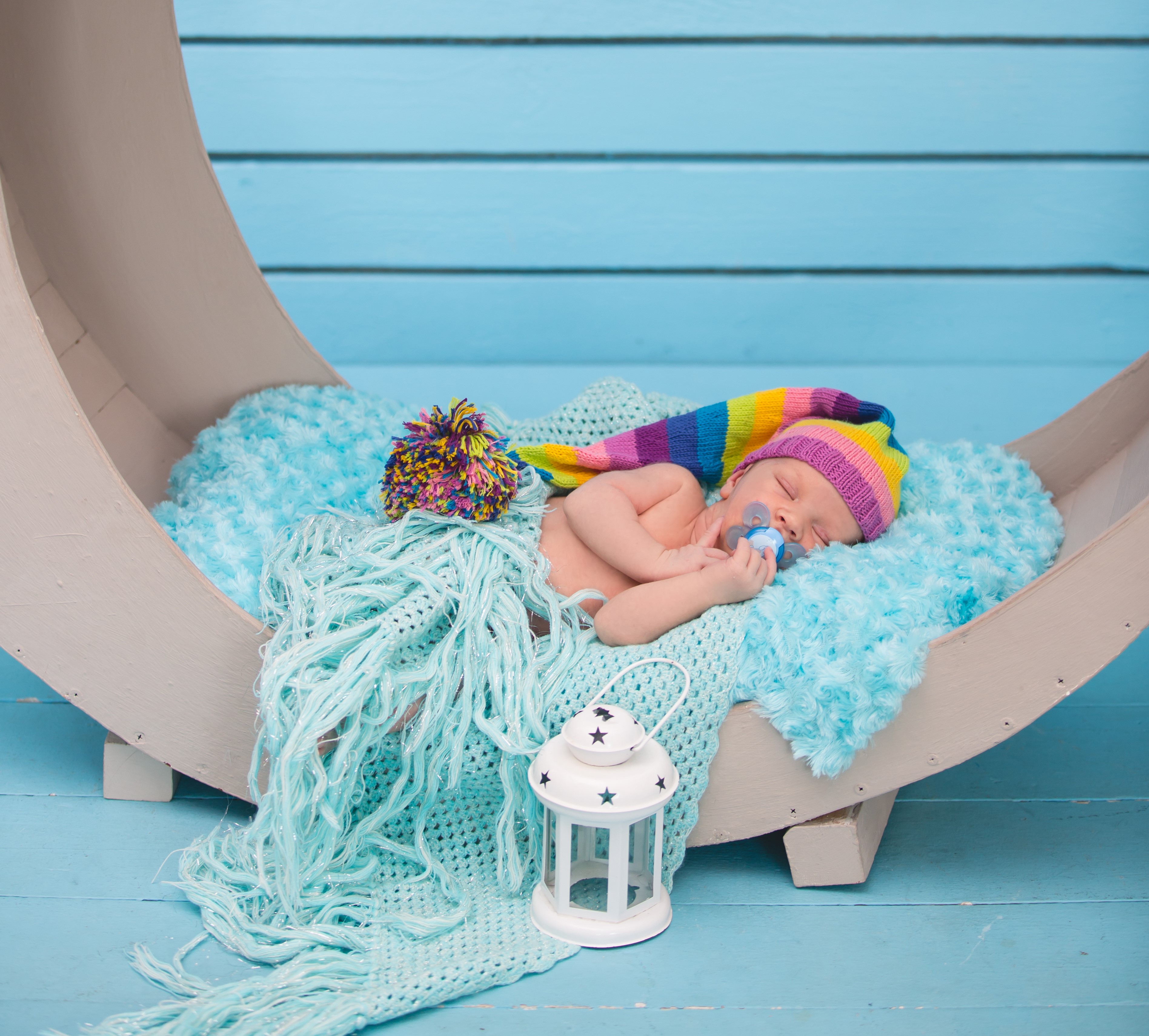 Newborn baby sleeping in a crescent moon prop with a rainbow hat HD Wallpaper