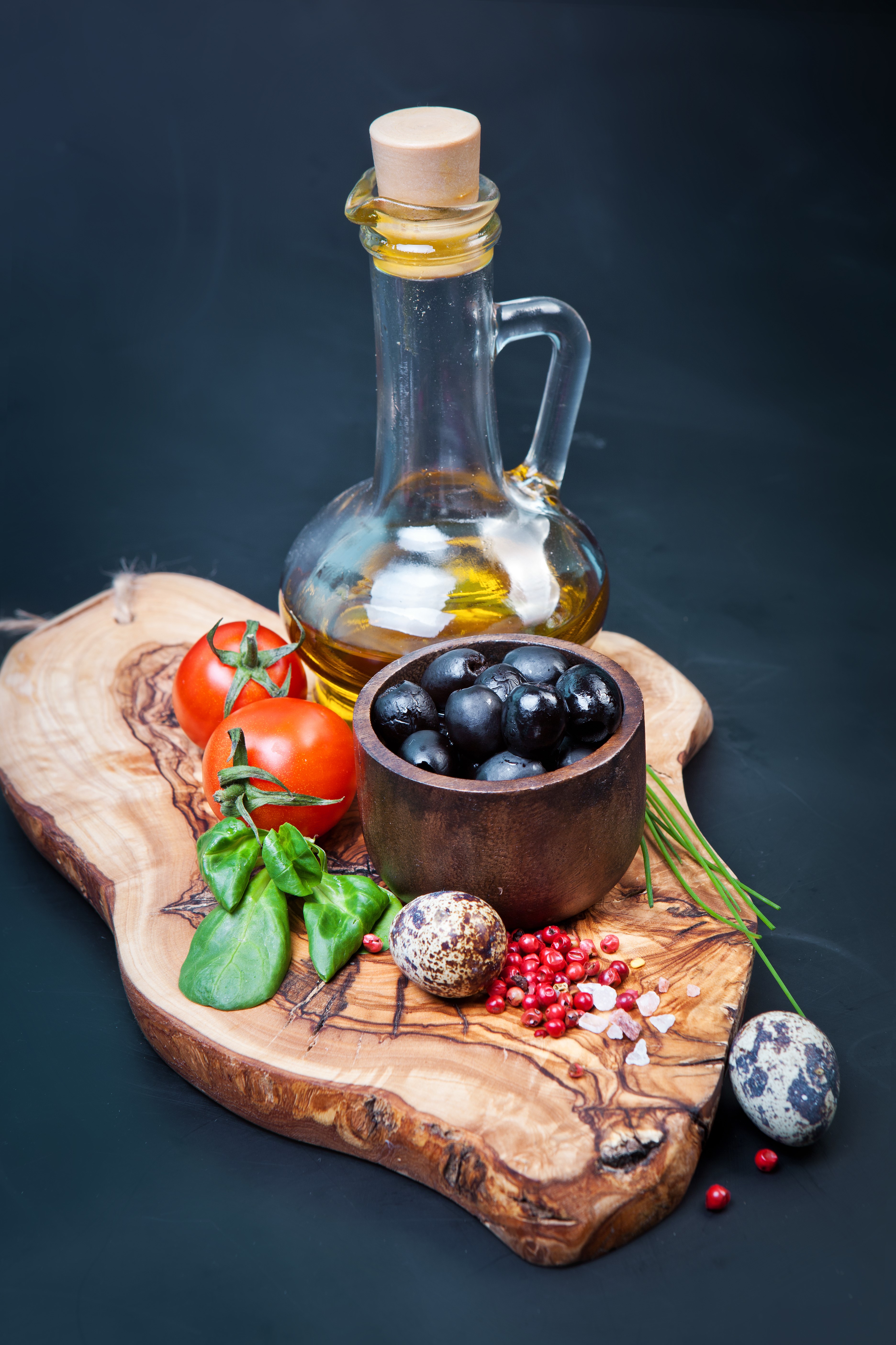 Olive oil bottle with tomatoes, olives, and quail eggs on a cutting board HD Phone Wallpaper