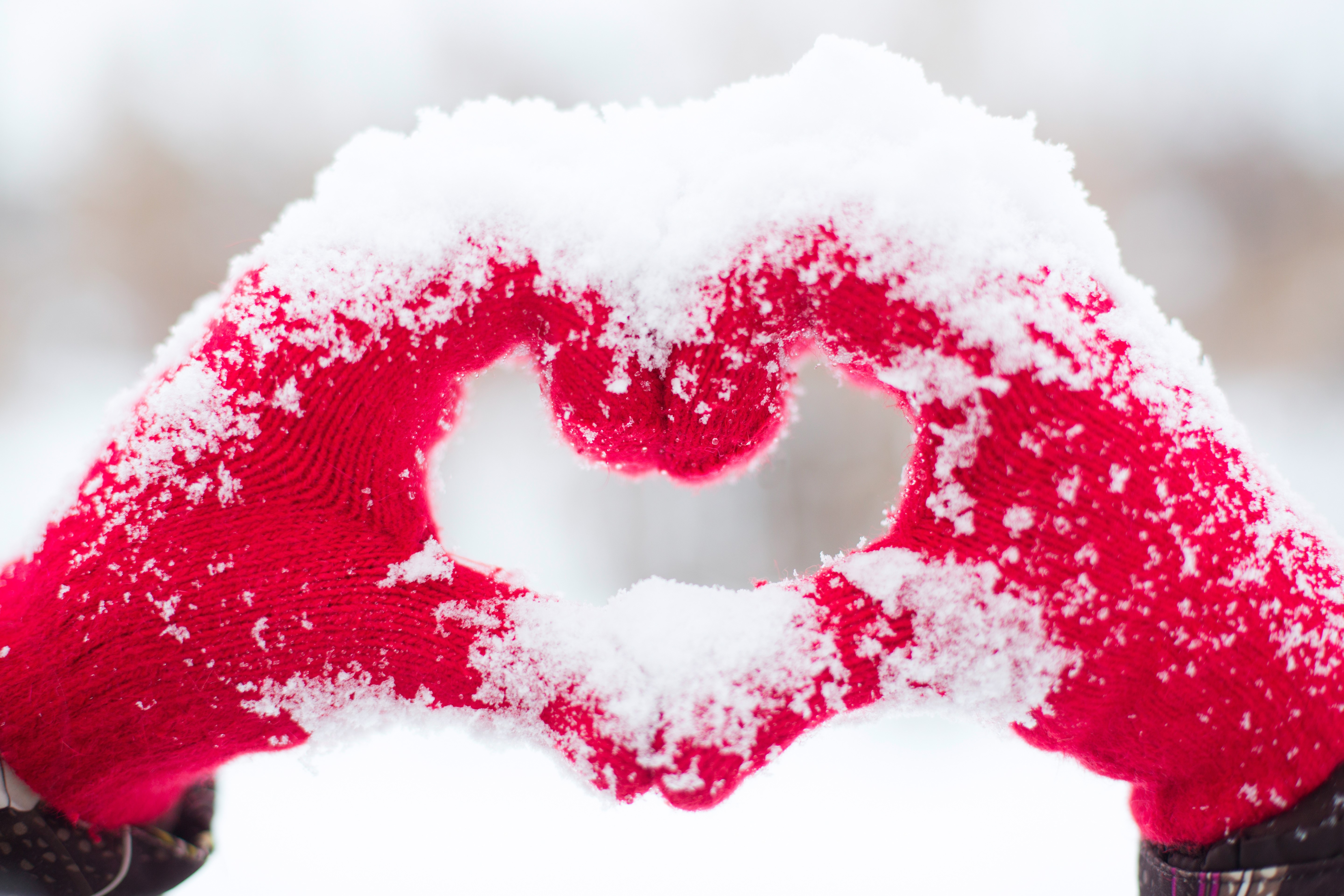 Hands in red gloves forming a heart shape in snow HD Wallpaper