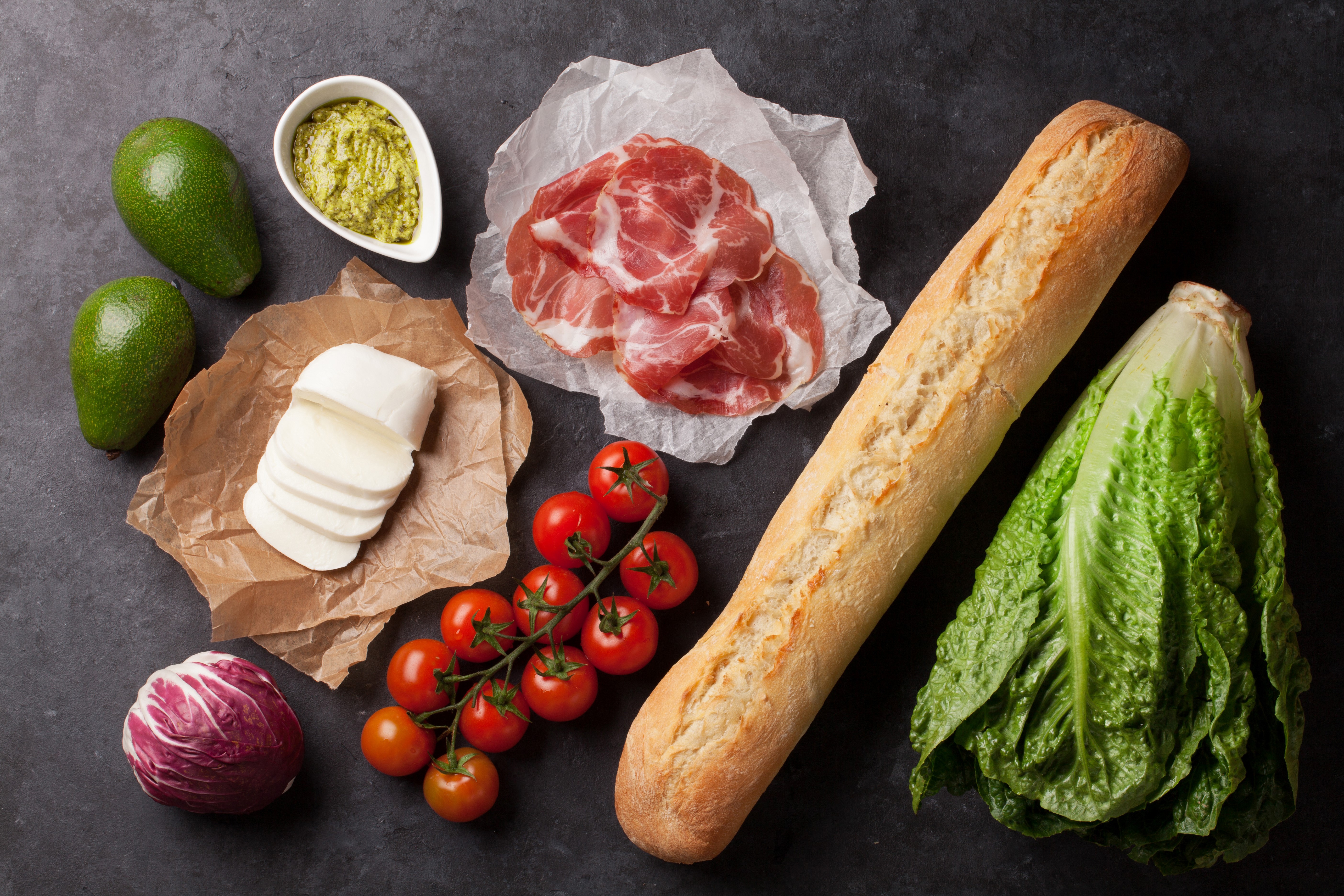 Still-life of sandwich ingredients: bread, ham, cheese, tomatoes, avocado, lettuce, radicchio, and pesto HD Wallpaper