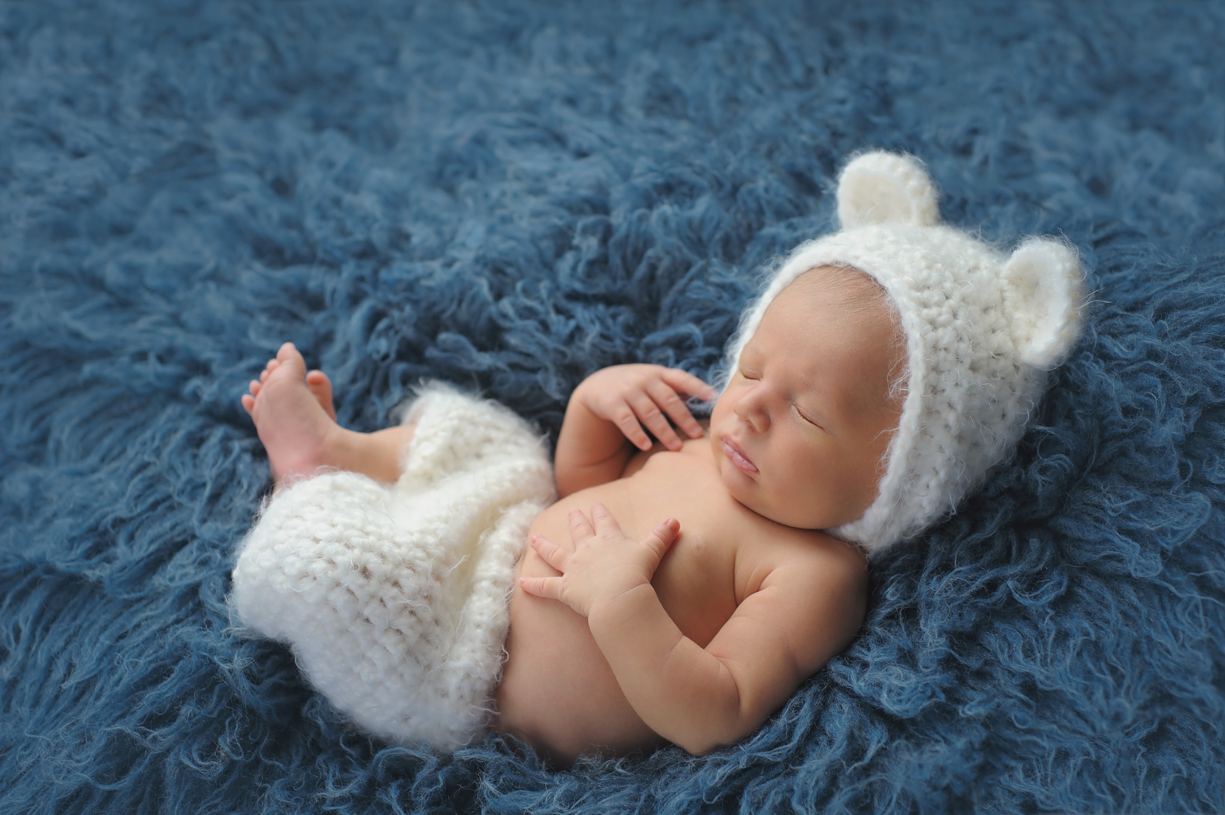 Baby in a bear hat sleeping on blue fur HD Wallpaper