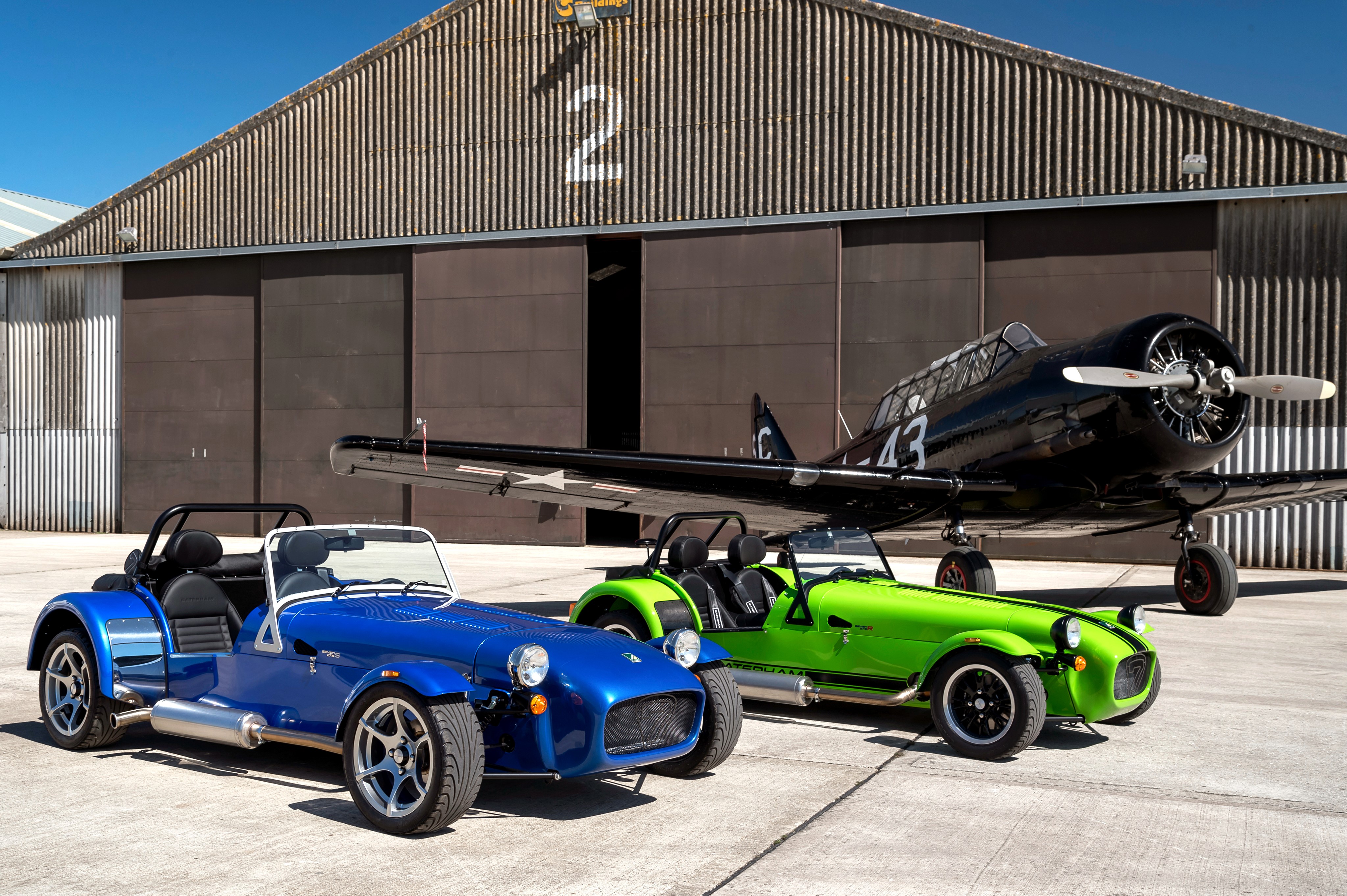 Two Caterham 7 cars and a vintage airplane HD Wallpaper