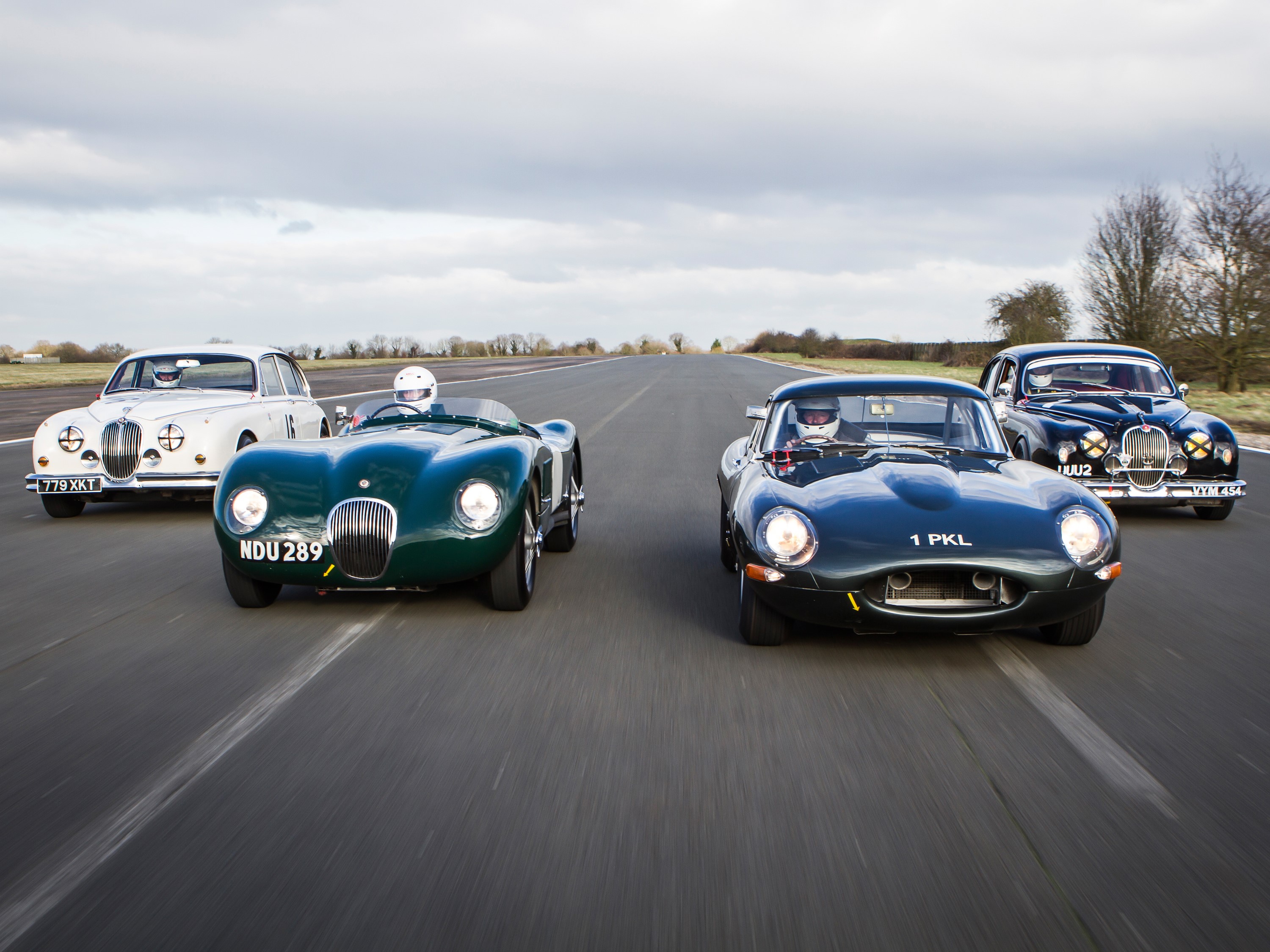 Four classic Jaguar cars driving on a road HD Wallpaper