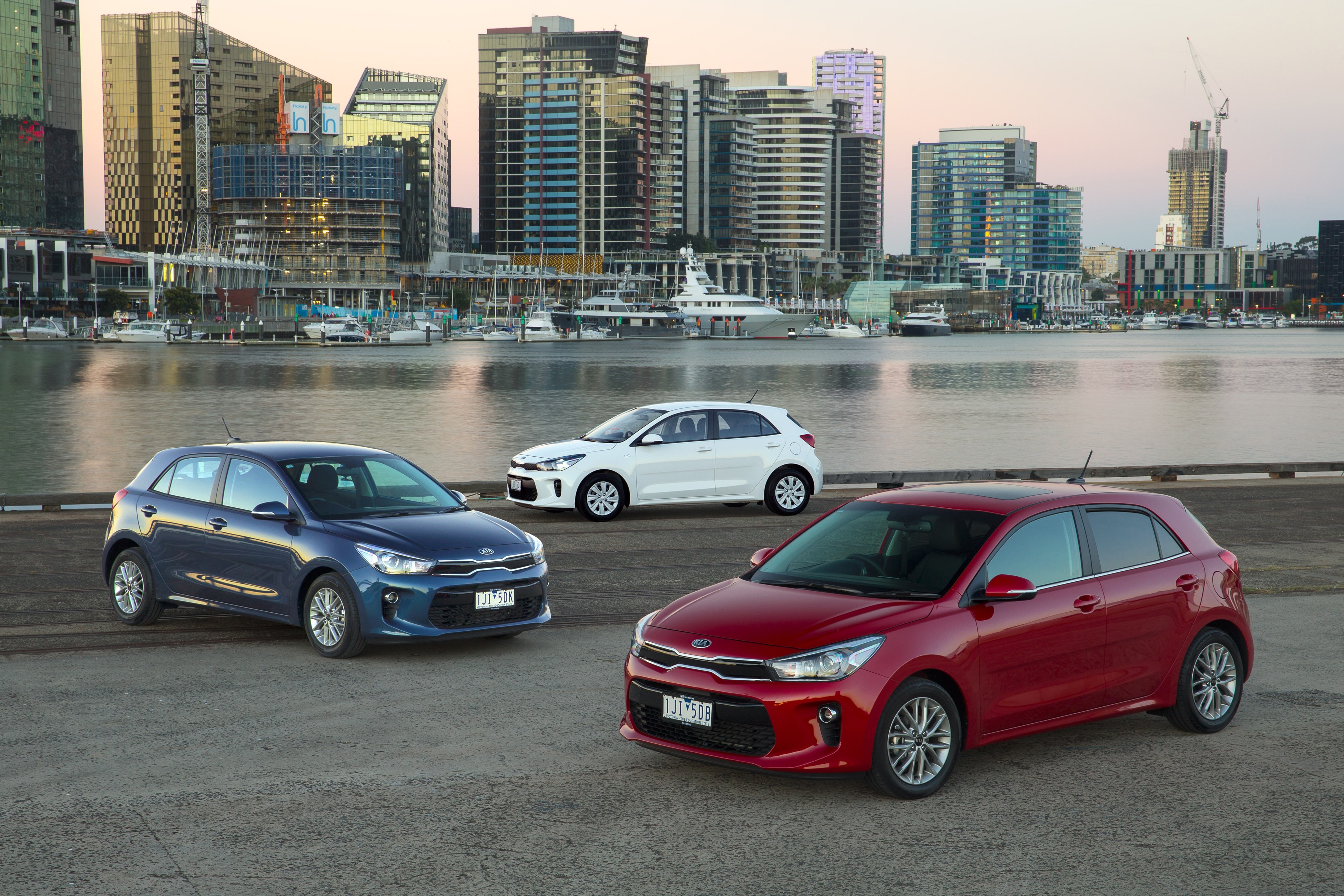 Three Kia Rio cars by the water with city skyline HD Wallpaper