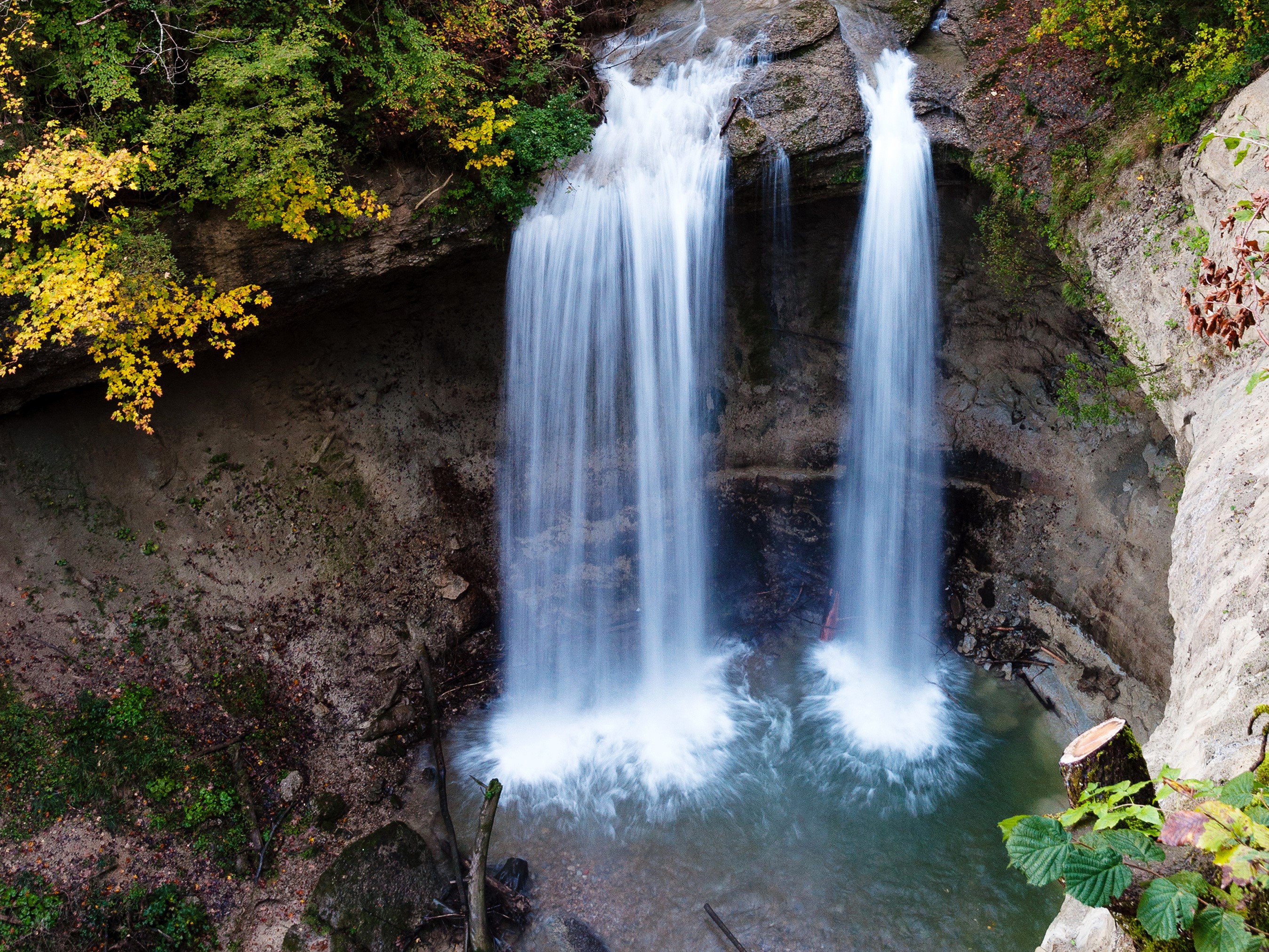 Twin waterfalls cascading into a pool in a rocky canyon HD Wallpaper