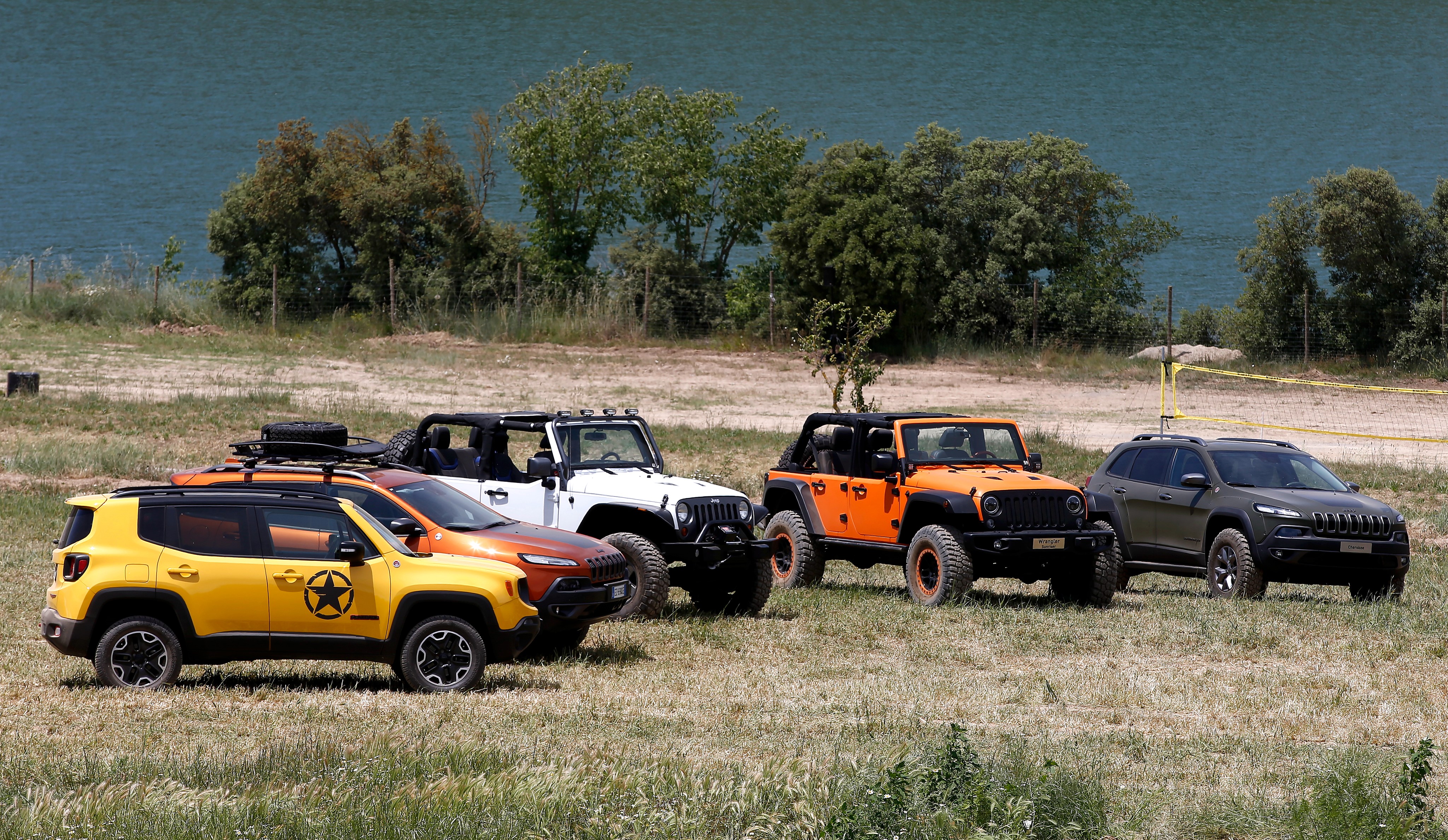 Four Jeeps parked on grassy terrain near a body of water HD Wallpaper